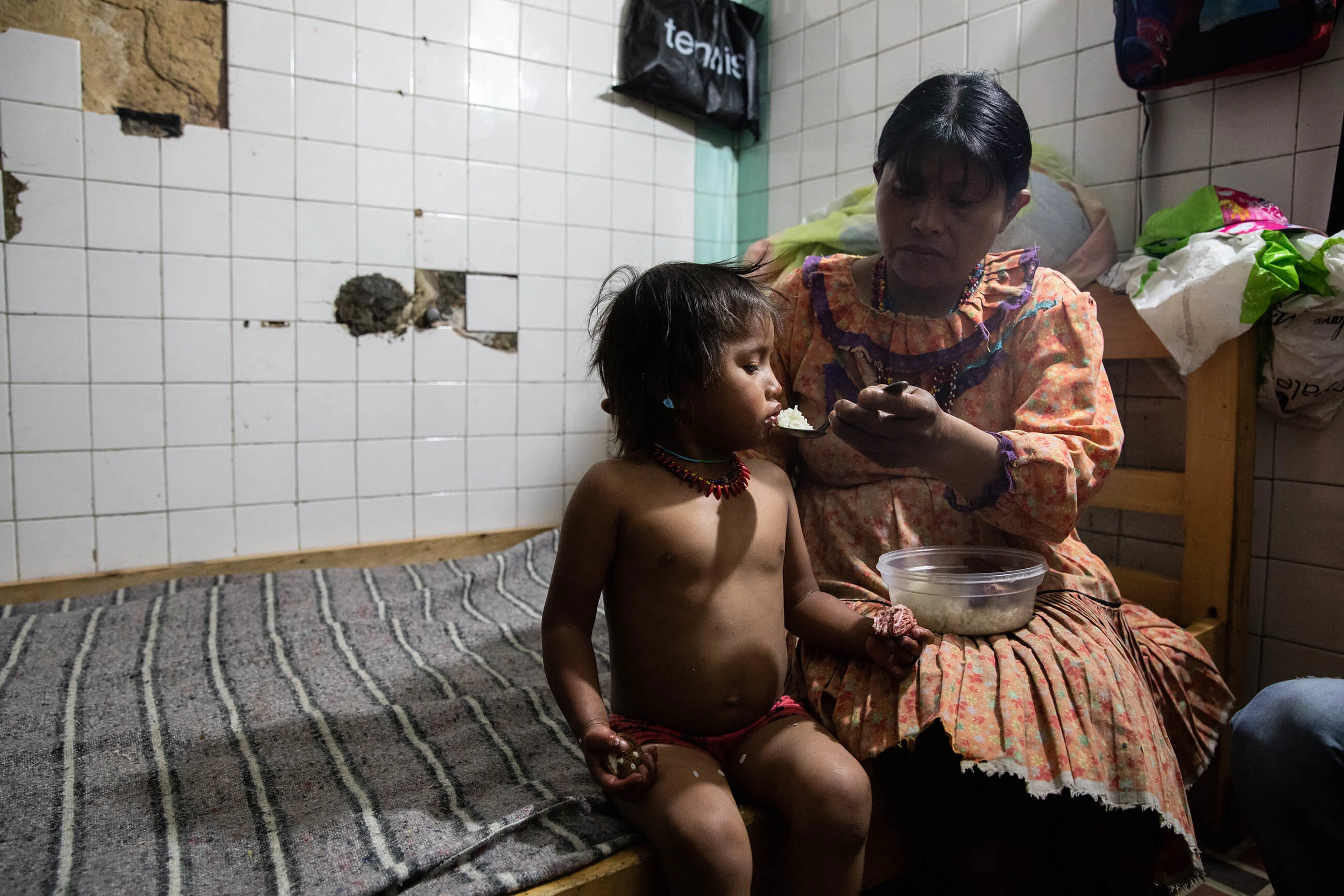 A displaced mother feeds her baby in a meat locker converted into a bedroom