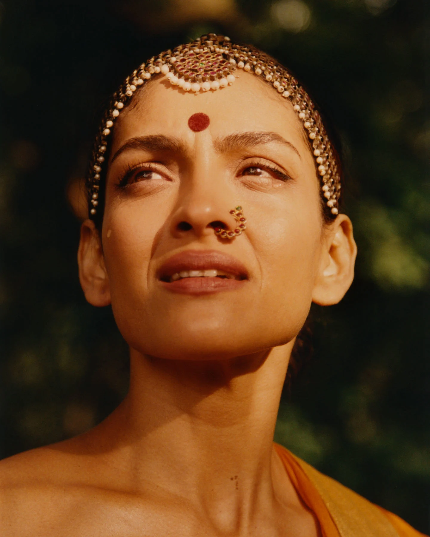 A close-up photograph of Bharatanatyam dancer Rukmini Vijayakumar, with golden rays of sunlight illuminating her face, revealing tears of reverence as she remembers the Hindu deity Shiva.