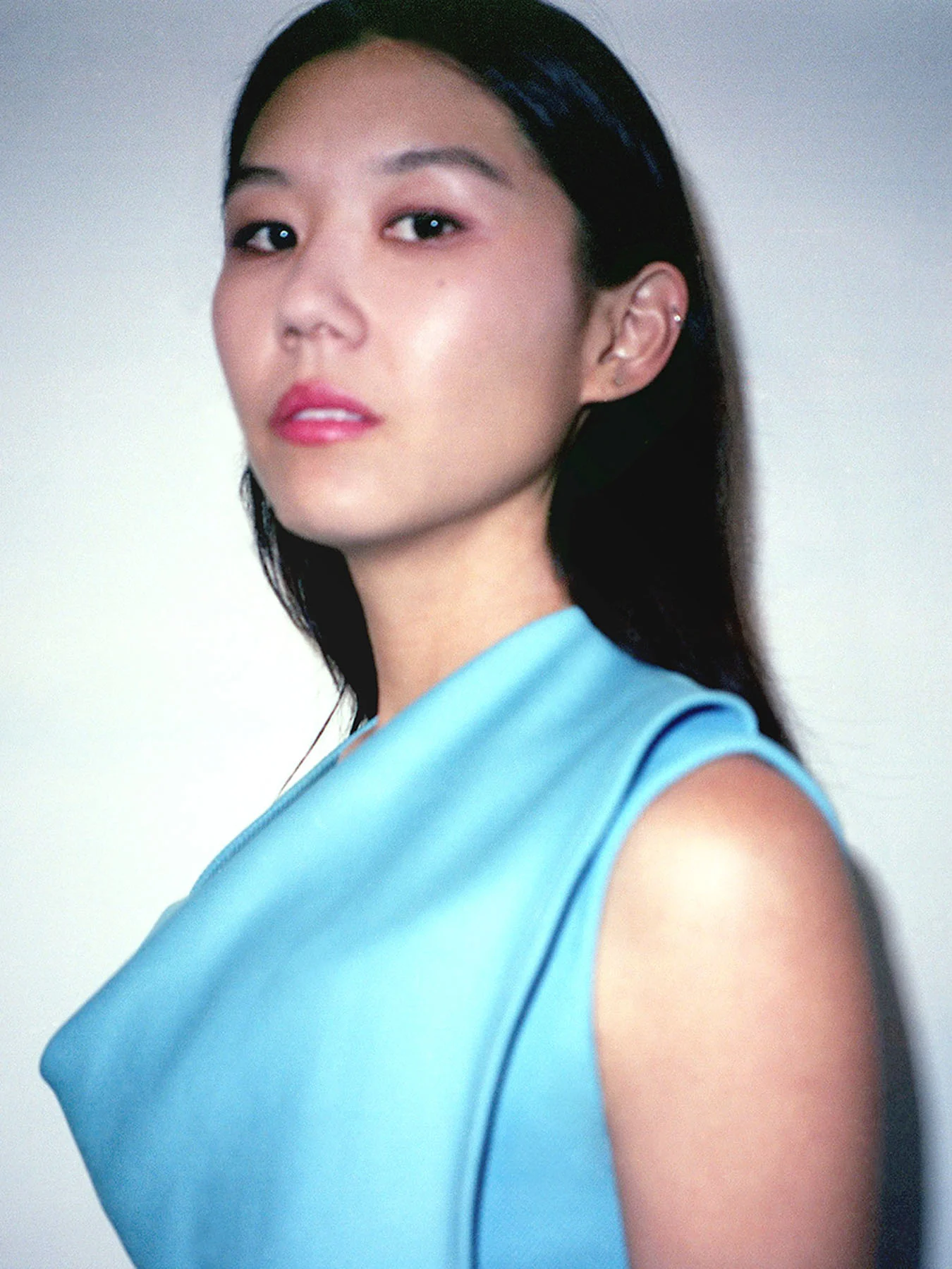 A woman stands facing the camera in a blue shirt.