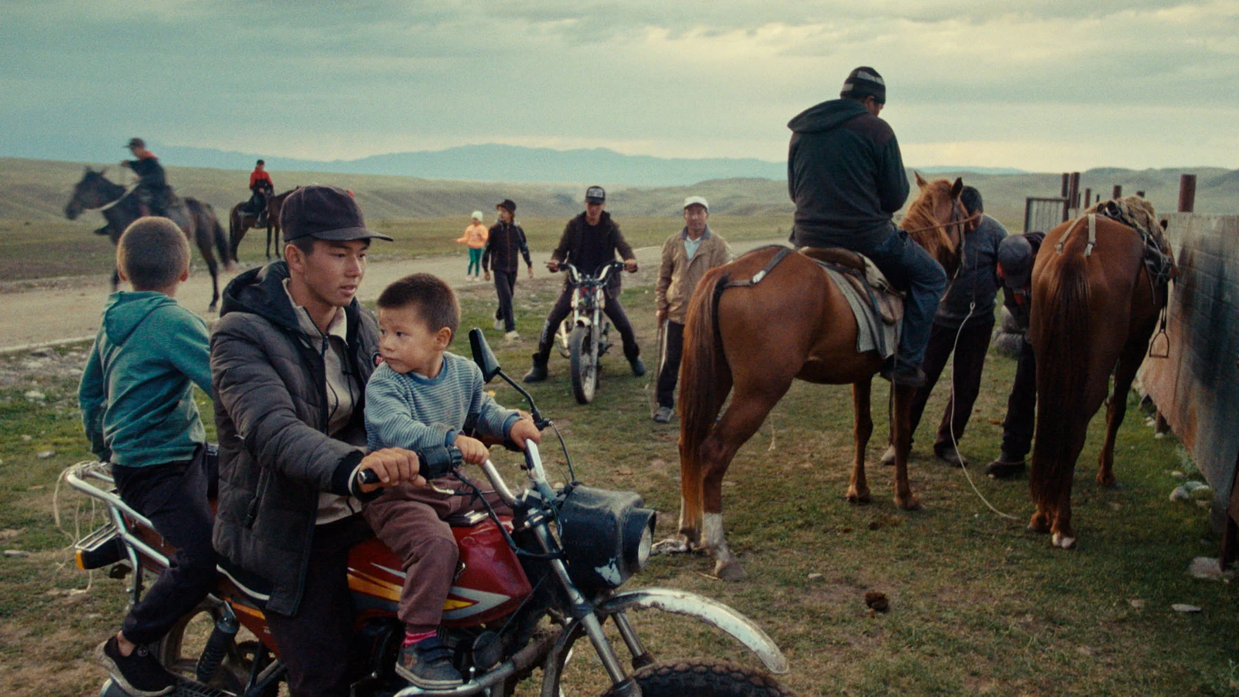 A still from the film “Astride” showing people on horses and motorcycles gathering next to a long road in the steppe of Kazakhstan. 
