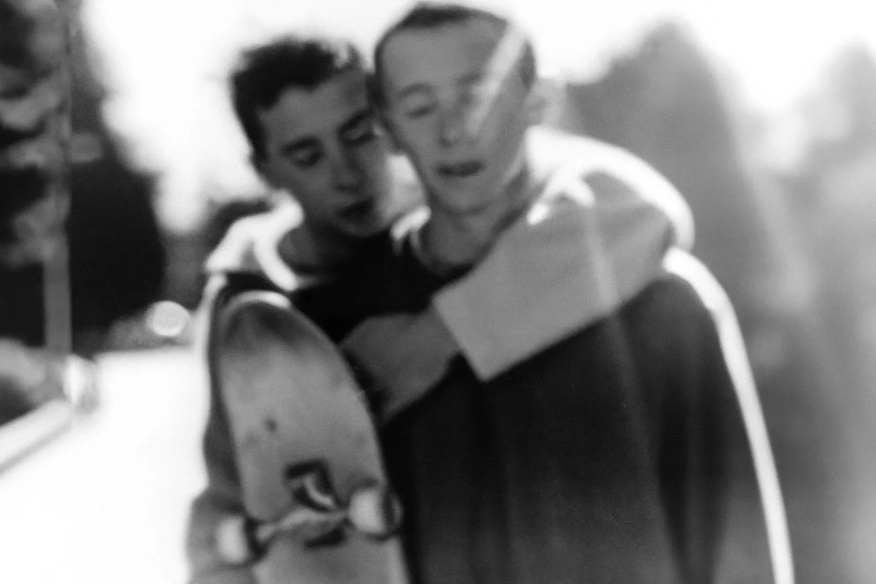 A black-and-white AI-generated photograph showing two people embracing, one with a skateboard in his hand, with sunlight shining into the camera’s lens from behind them