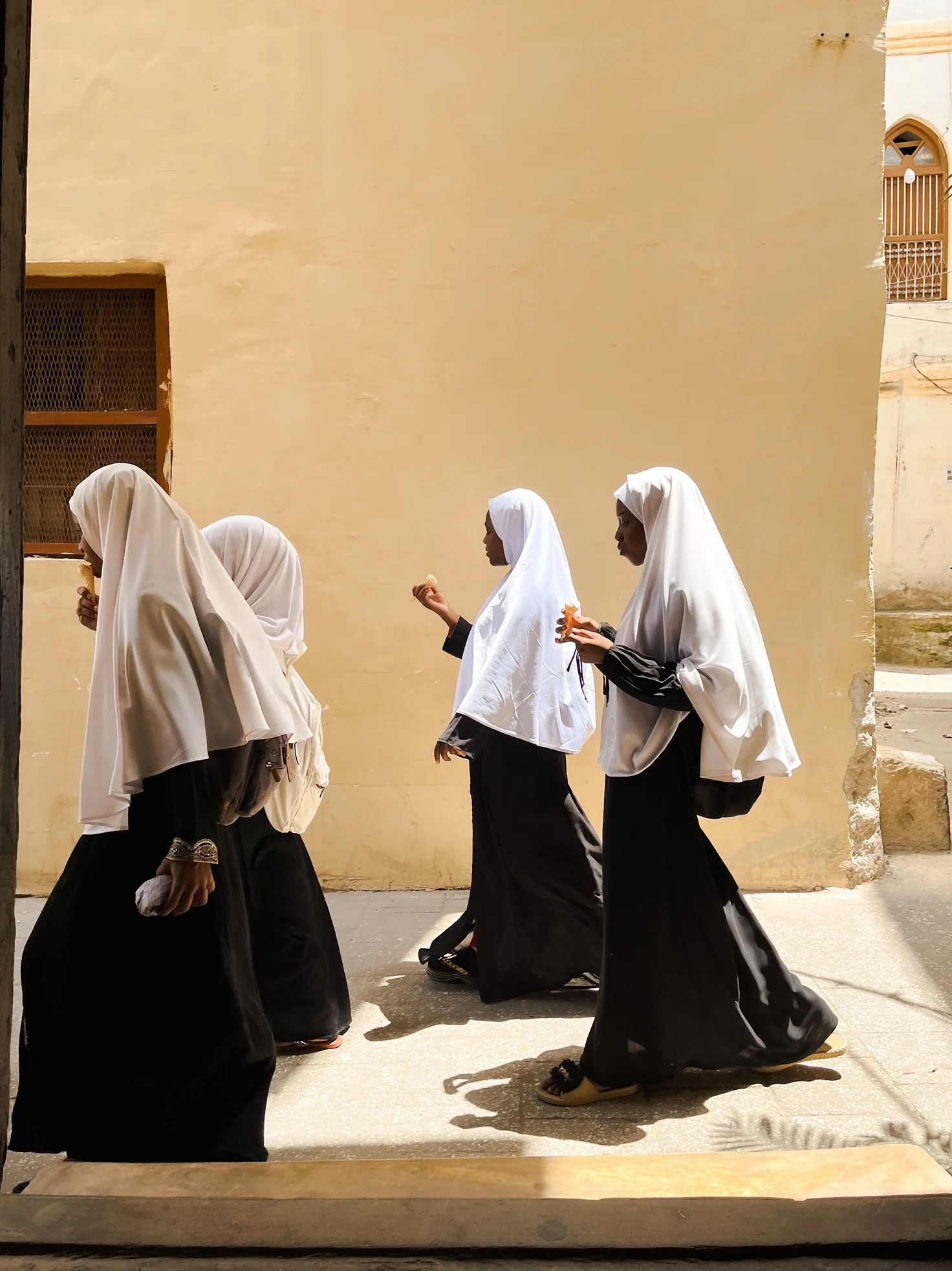 A photograph of four girls walking throigh a narrow street in Zanzibar, Tanzania.