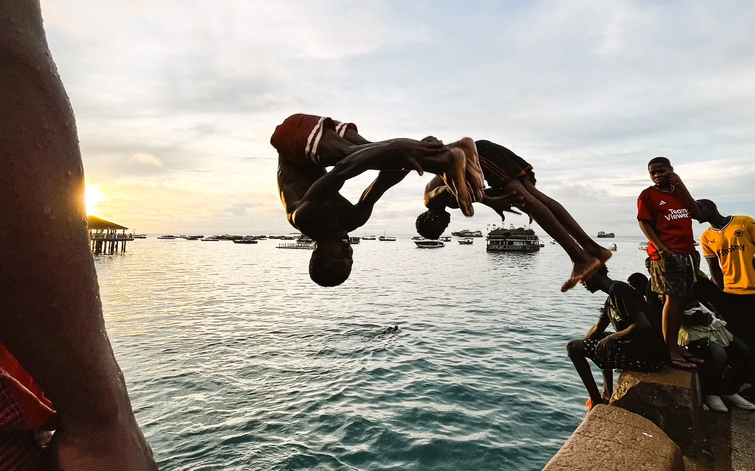 A photograph of two boys jumping off a wall into the sea in Zanzibar, Tanzania. 