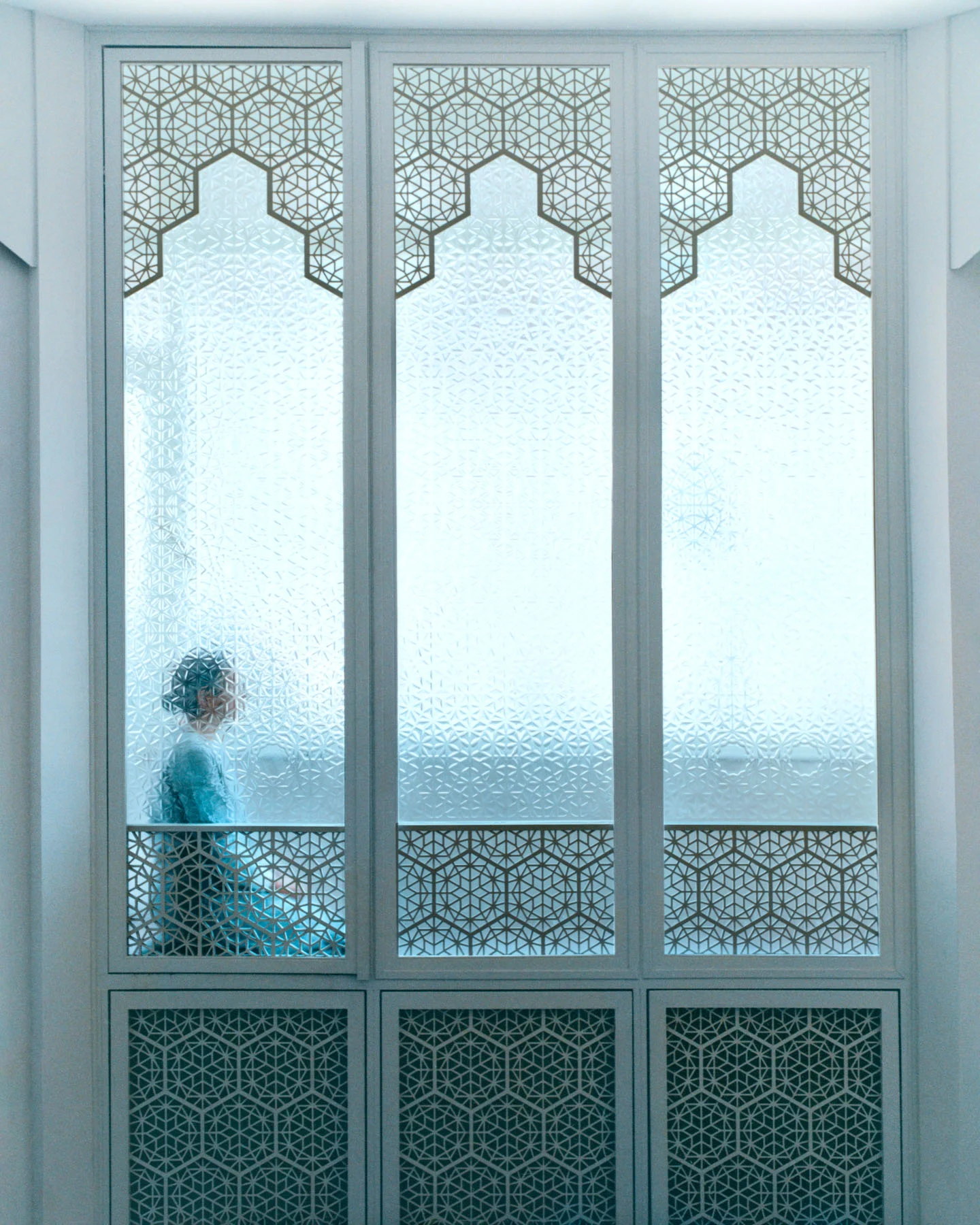 A photograph of architect Nevine Nasser sitting in meditation behind a decorative window with Islamic geometric motifs, at the Sufi centre she designed for her order.