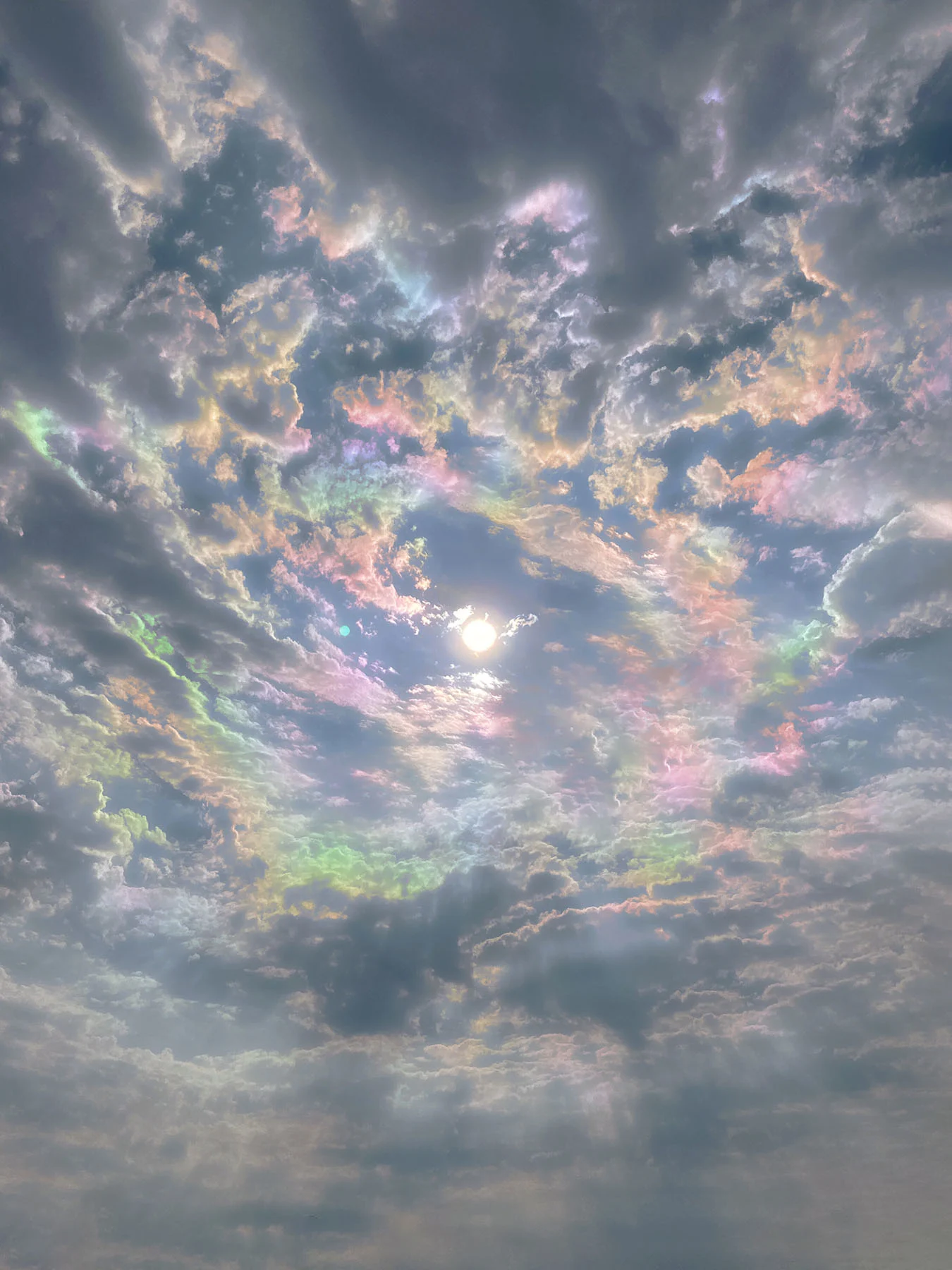A photograph of iridescent clouds spiraling inward towards a solitary sun.