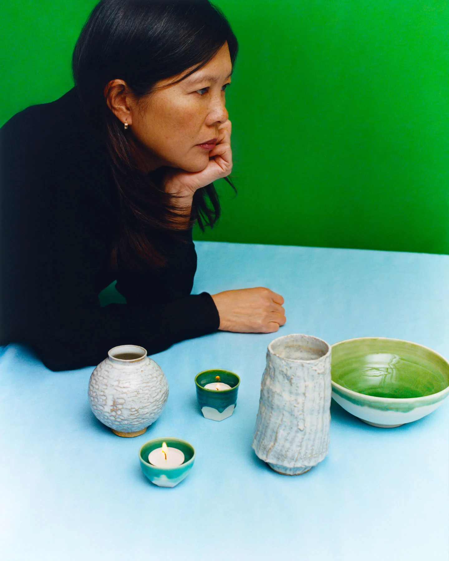 A photograph of ceramicist Sassirika Lam leaning on a table displaying some of her ceramic works.