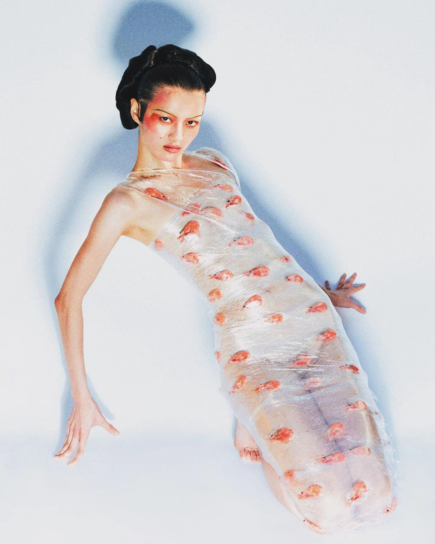 A photograph of model Wang Yuanxiang wearing a dress made from cling film, with shrimp wrapped inside its layers.
