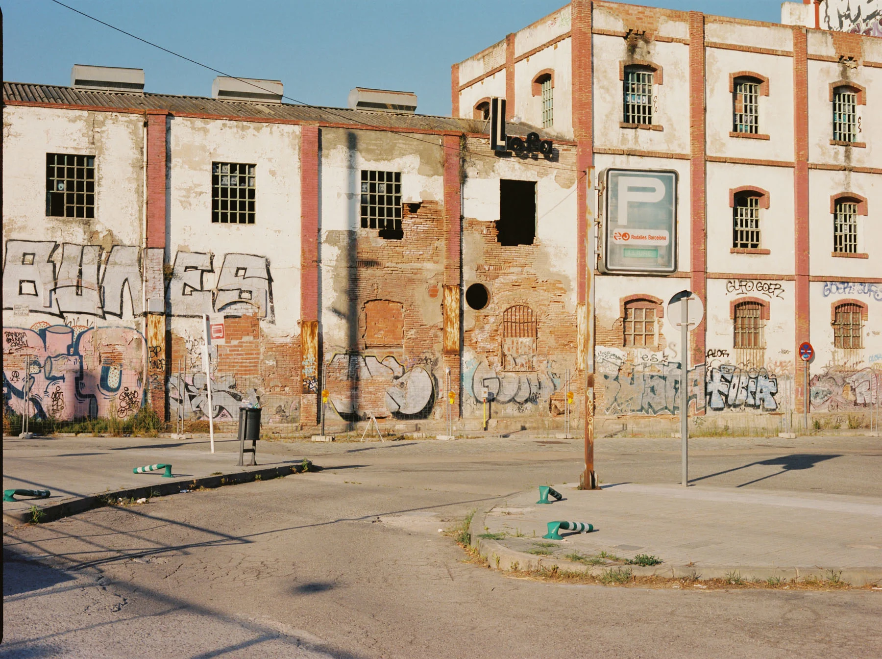 A photograph of an abandoned warehouse. The walls of the warehouse are painted with graffiti. There is also a parking sign which pointing to the train station beside the warehouse.