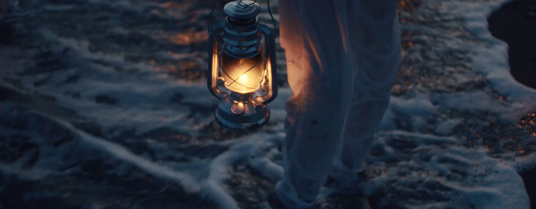 An extract from the film "Blue Eyes by Andre Muir," showing a group of people slowly walking into the sea, holding lanterns.