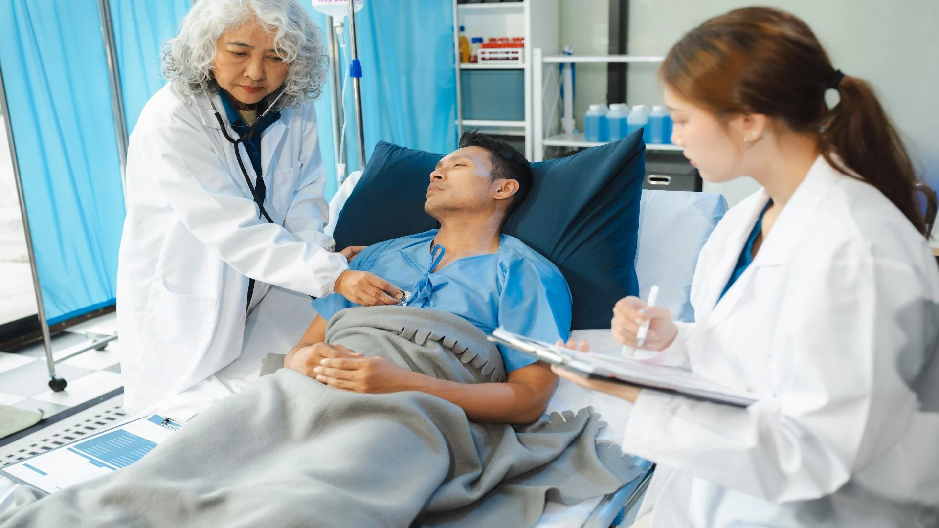 older female doctor checking male patient's vitals as a nurse takes notes.