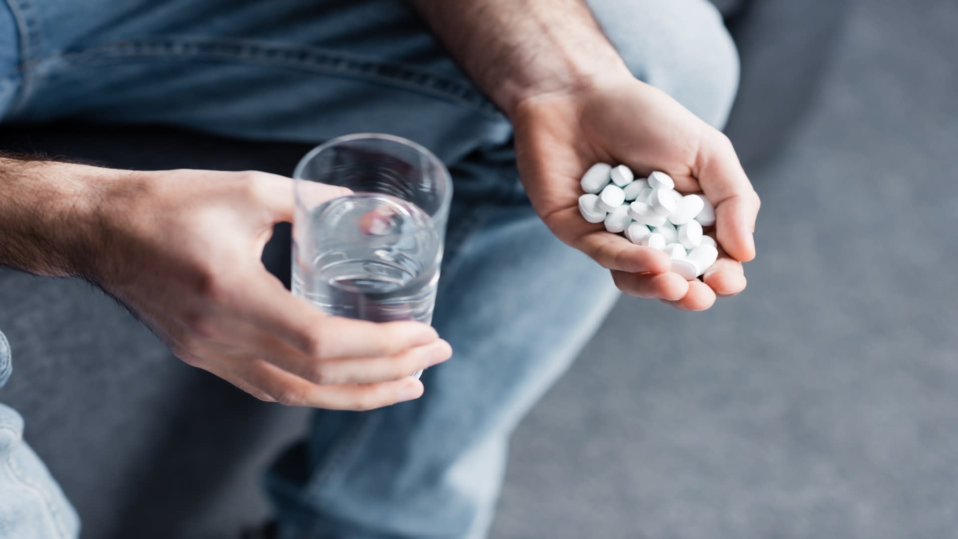 Synthetic opioids in a man’s hand next to a glass of water, showing a moment of contemplation or crisis.