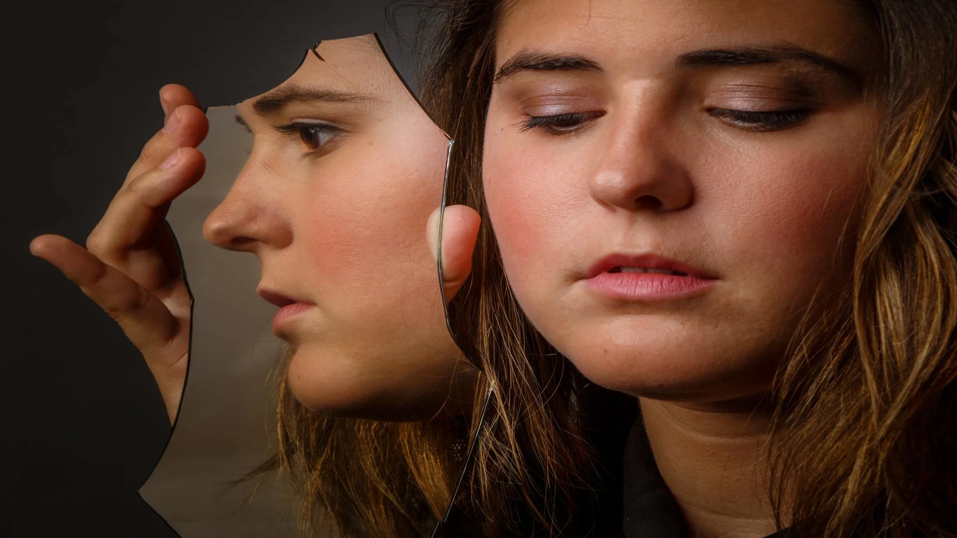 Woman examining her reflection in a broken mirror, symbolizing fractured perception and emotional turmoil—how a person with bipolar thinks during self-reflection.
