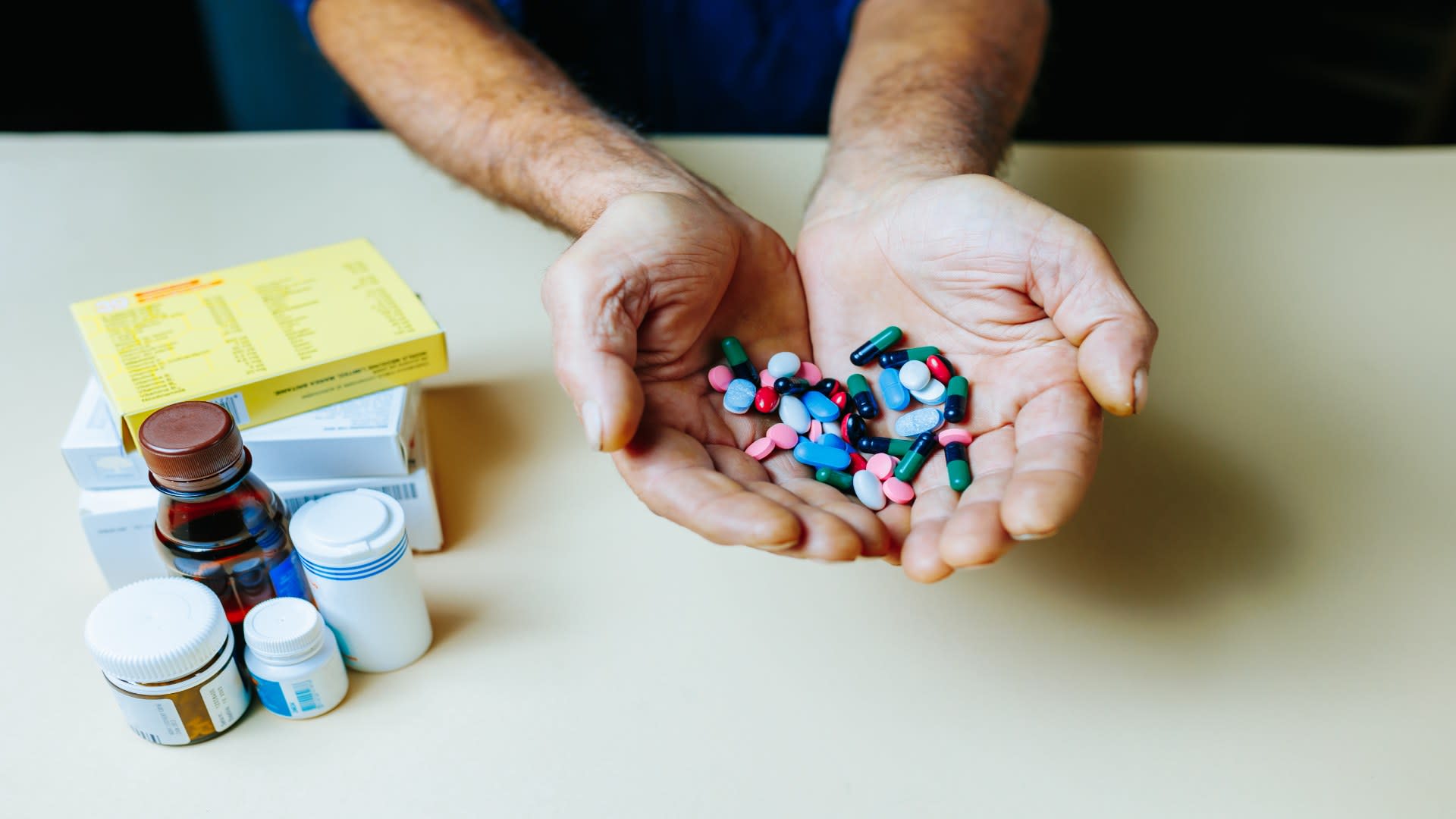 A person holds a large handful of colorful capsules and tablets, surrounded by medication containers—highlighting the need to understand what are benzodiazepines and how they differ from other drugs.