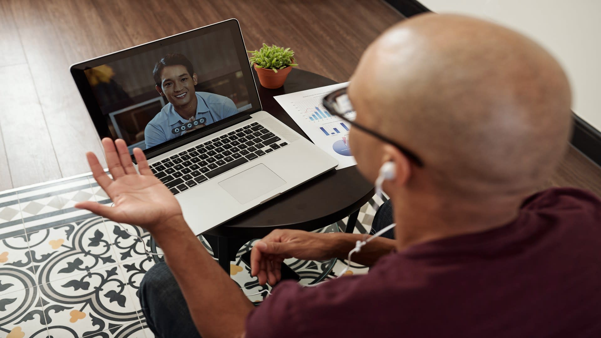 Man engaging in online therapy for PTSD, using a laptop and earbuds for a video call with a mental health professional.