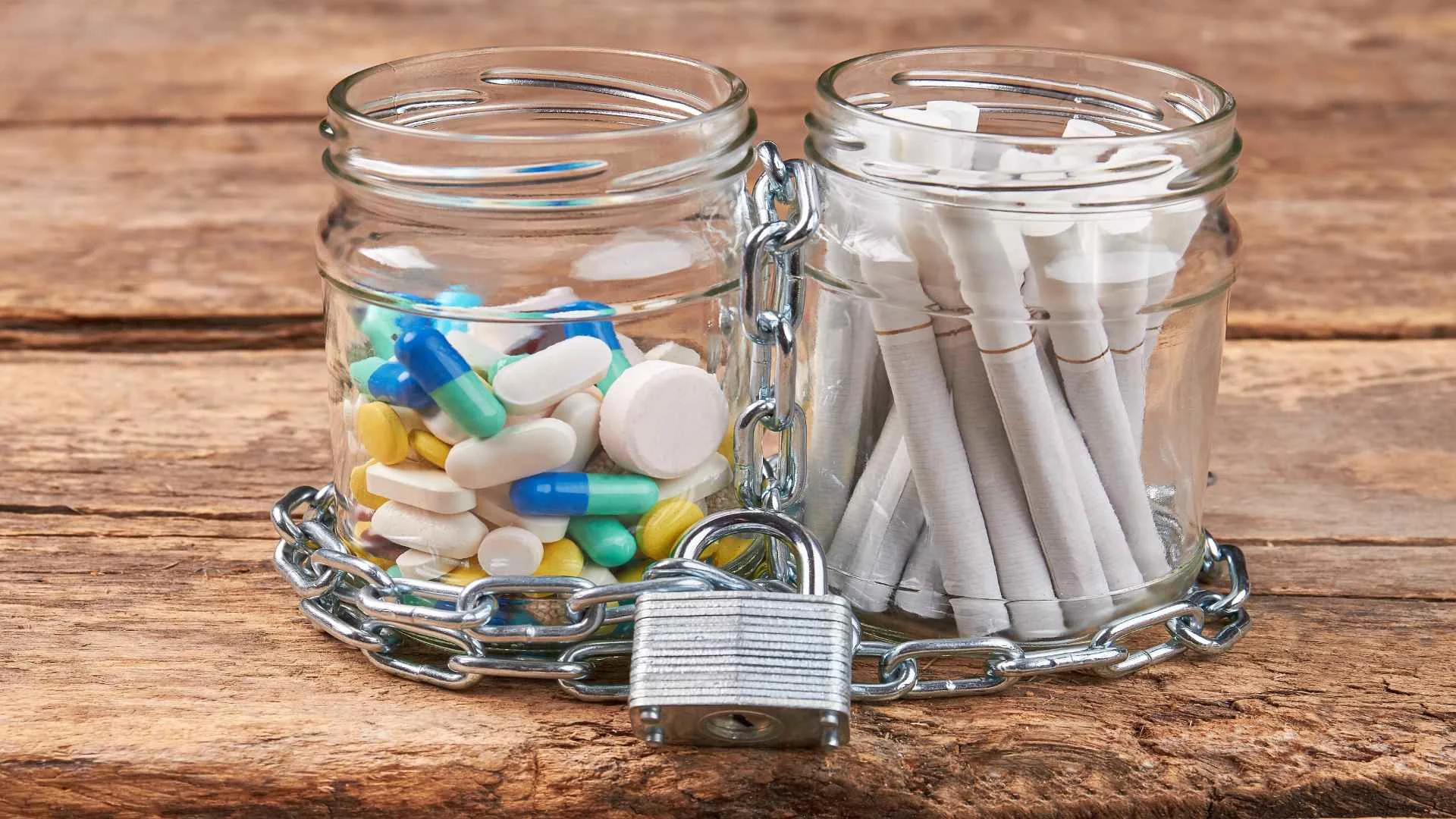 Glass jars filled with cigarettes and pills chained and locked, symbolizing the struggle with substance abuse often rooted in attachment issues.