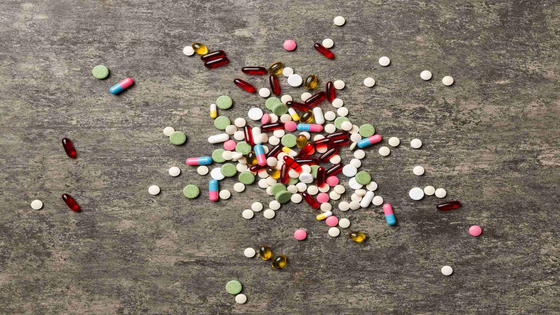 Benzodiazepines list visually represented by a colorful mix of pills and tablets on a concrete background, symbolizing the variety and availability of prescription sedatives.