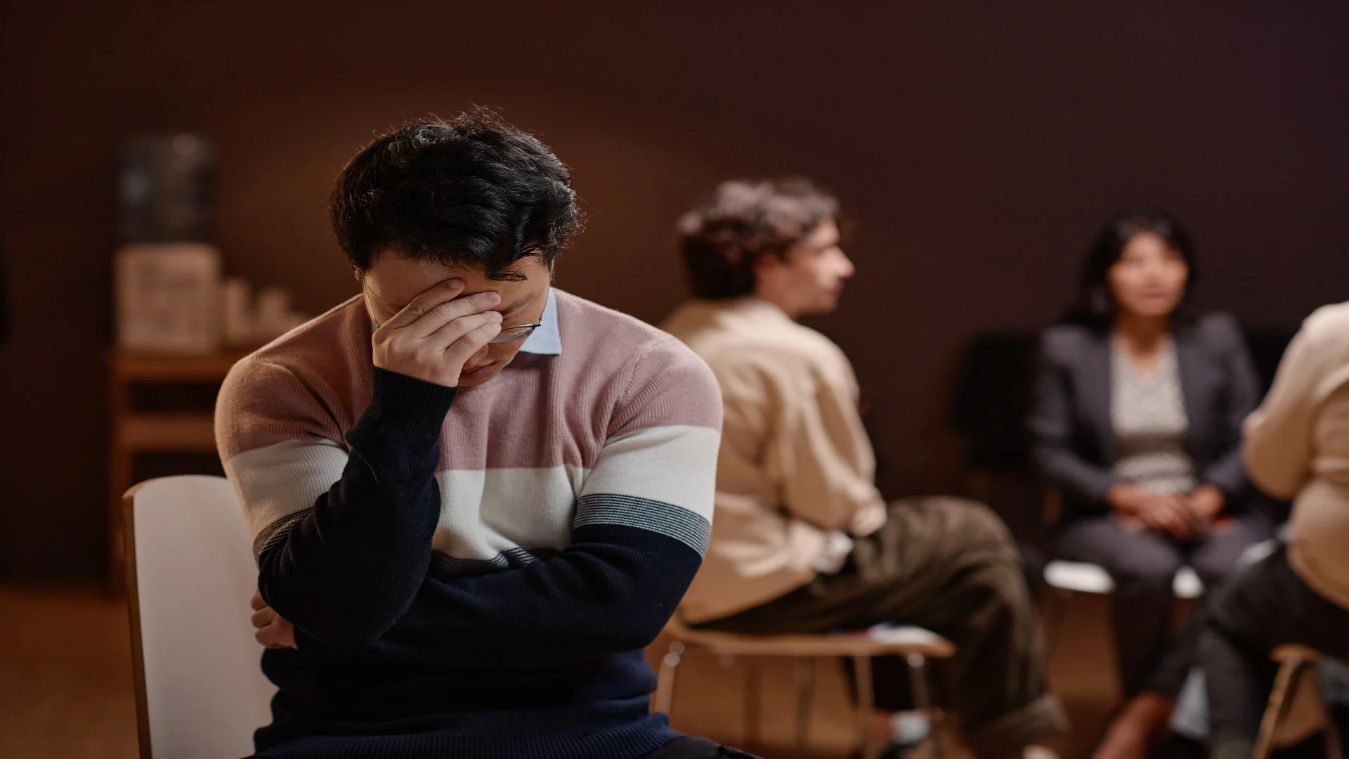 Man holding his face in distress during a support group, illustrating the emotional burden of depression and the importance of knowing how to help someone with depression.