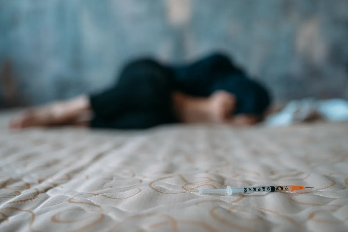 Fentanyl Addiction: Blurry picture of a man curled up with a needle in frame