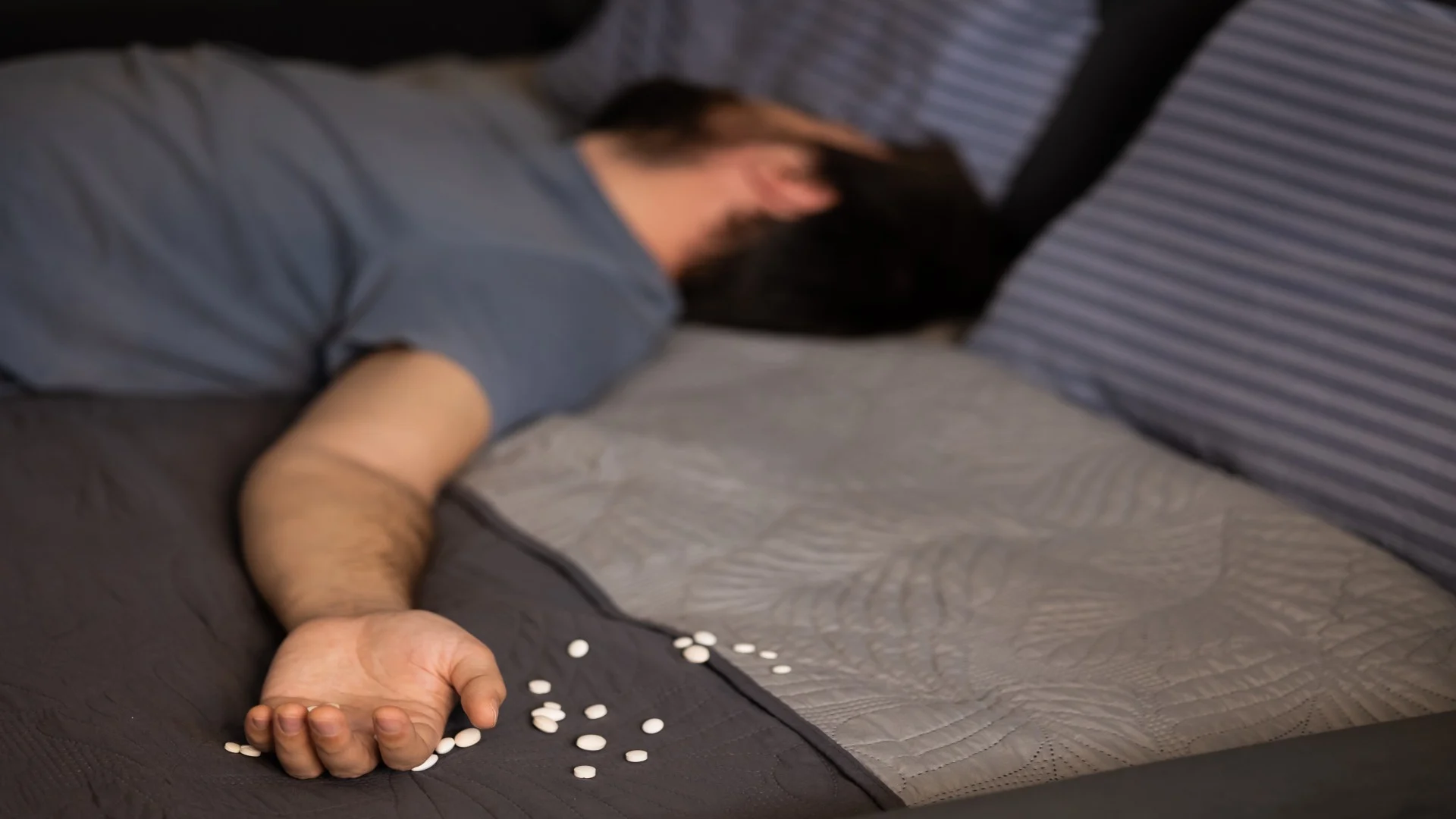 Unconscious man lying in bed with scattered pills, symbolizing overdose risk and the question Is ketamine addictive.