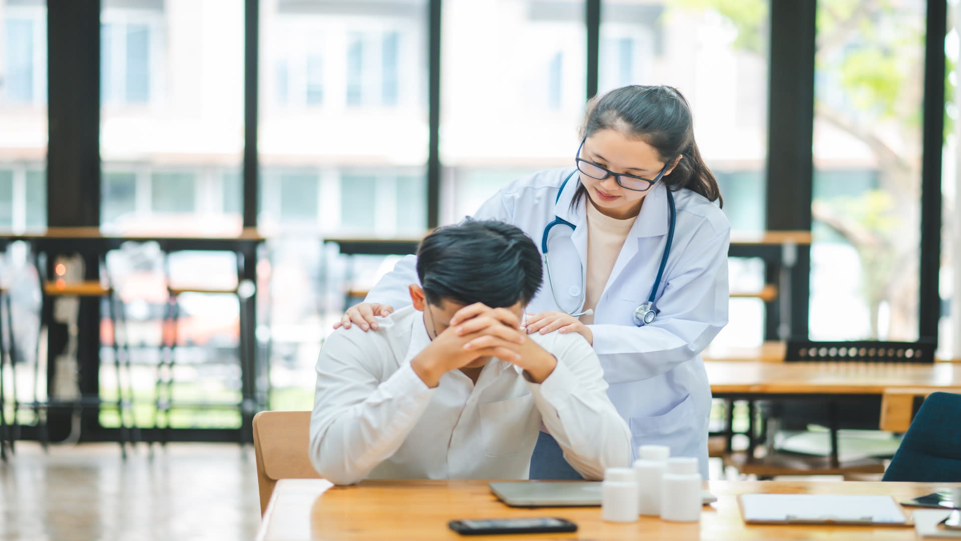 A doctor places a comforting hand on a man’s shoulder as he sits with his head down, highlighting the importance of empathy and connection when assisting someone with depression.