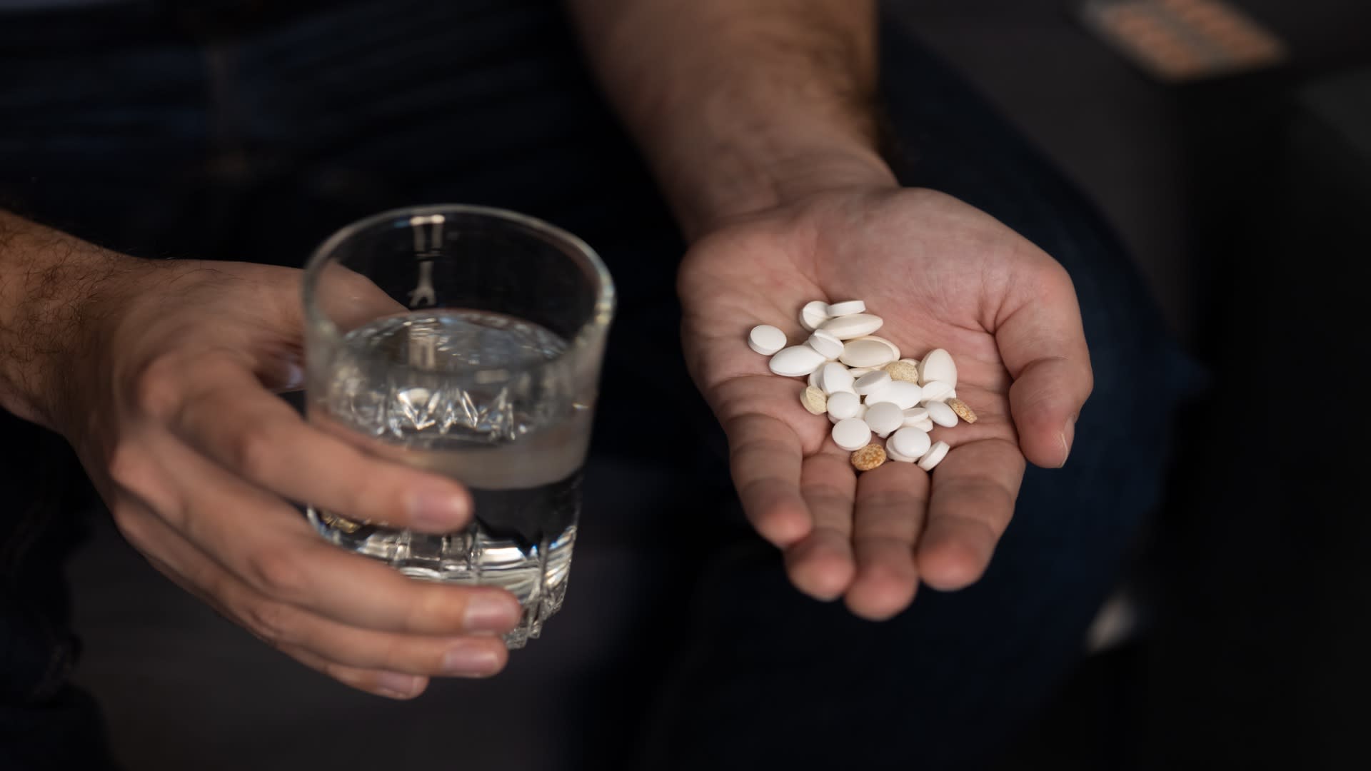 Close-up of a person holding multiple pills and a glass of water, representing potential hydrocodone misuse or overmedication.