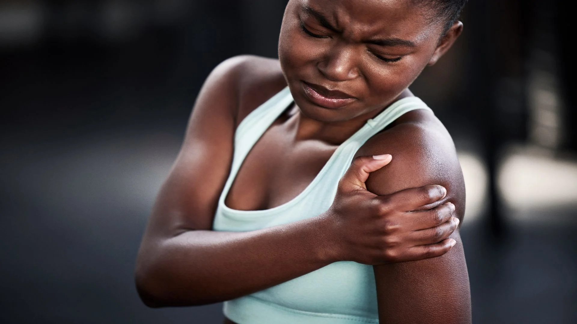 Young black woman athlete holding her shoulders in pain