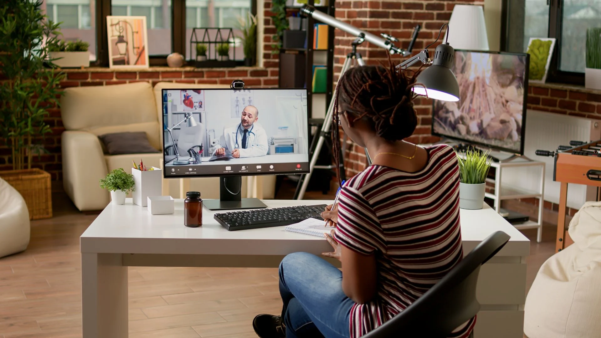 Young woman taking notes while speaking to a specialist in an online addiction counseling session at home.