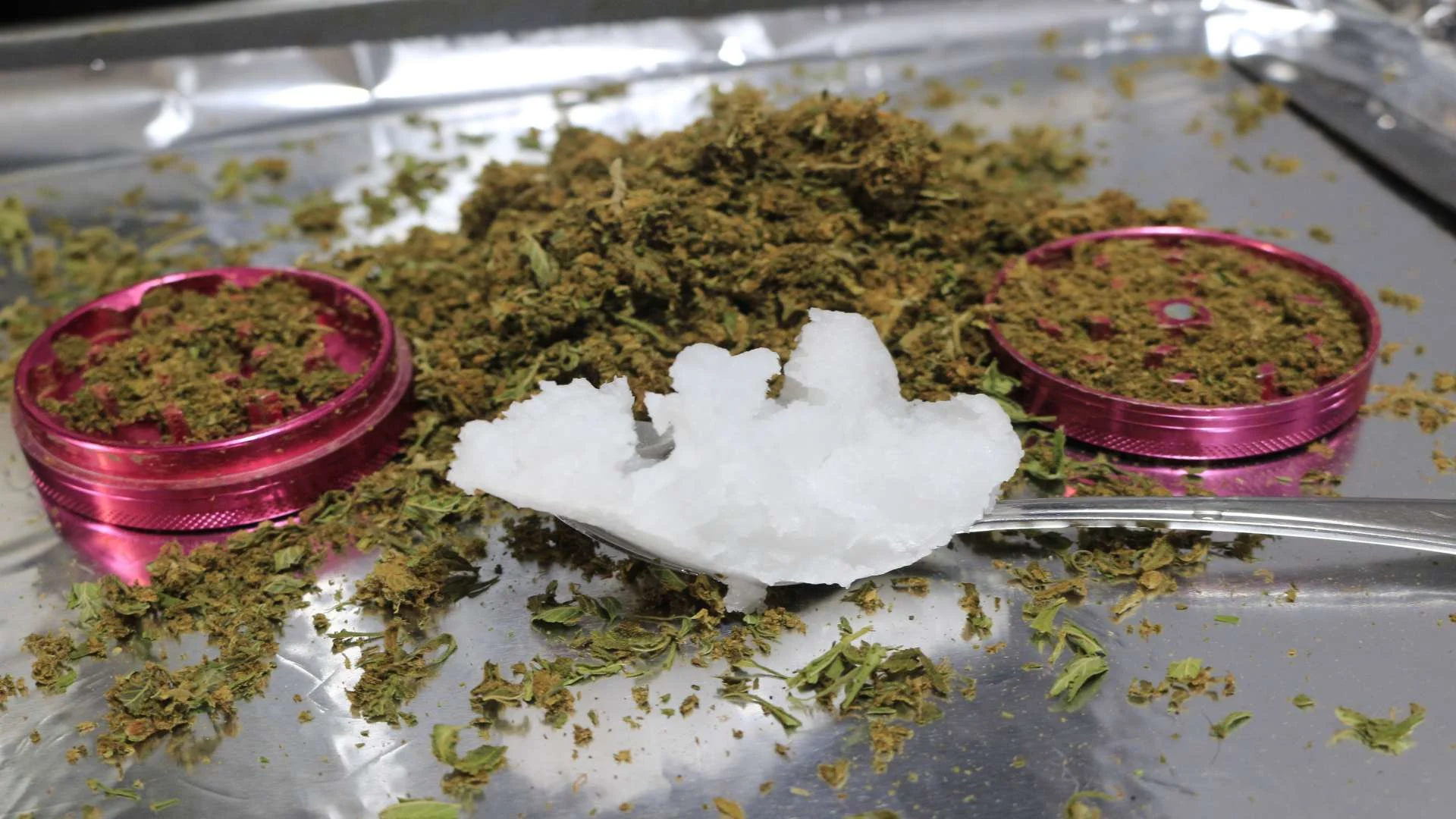 THC-O infusion preparation shown with coconut oil on a spoon next to ground cannabis and a pink grinder.