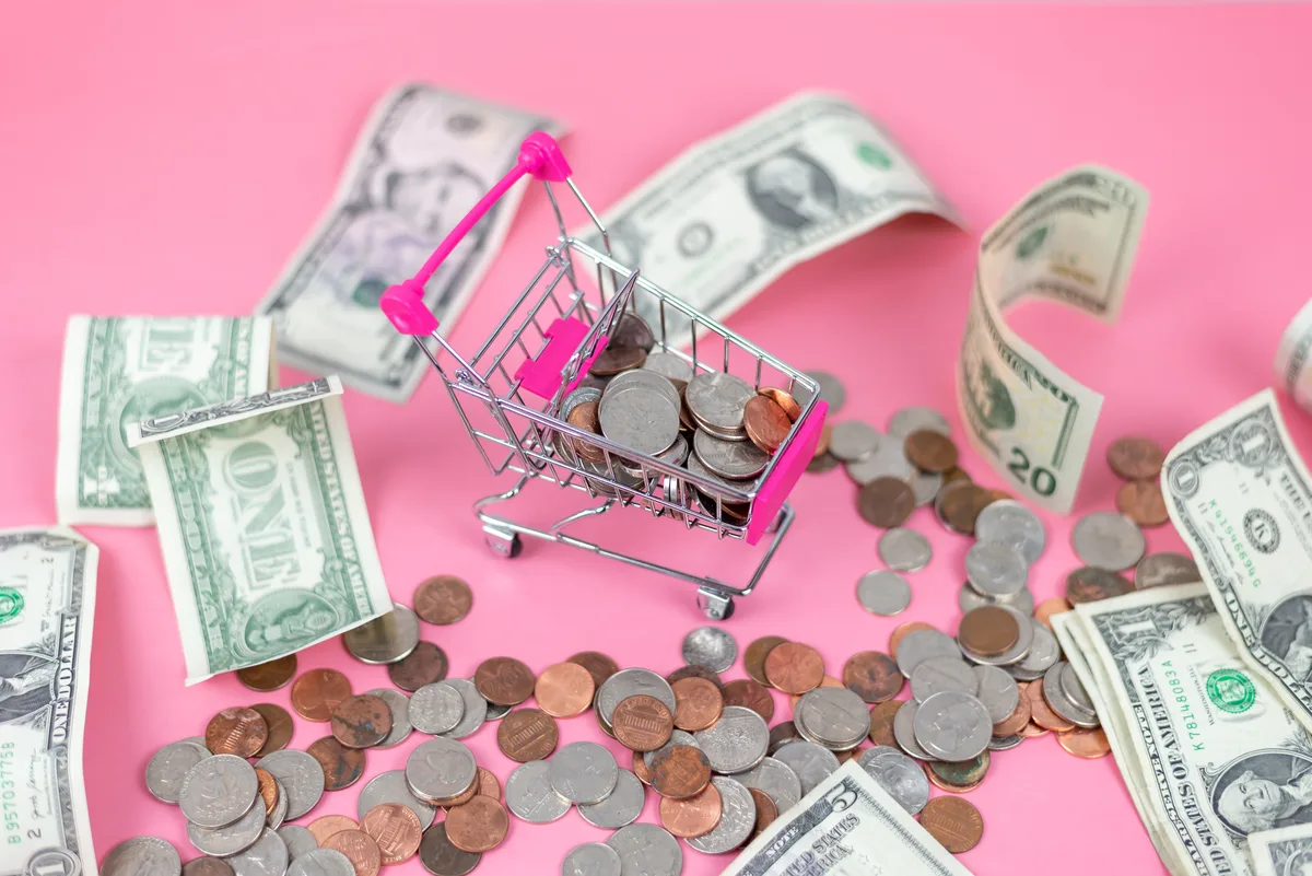 Shopping Addiction: Miniature shopping cart filled with coins and dollar bills Shopping Addiction: Miniature shopping cart filled with coins and dollar bills