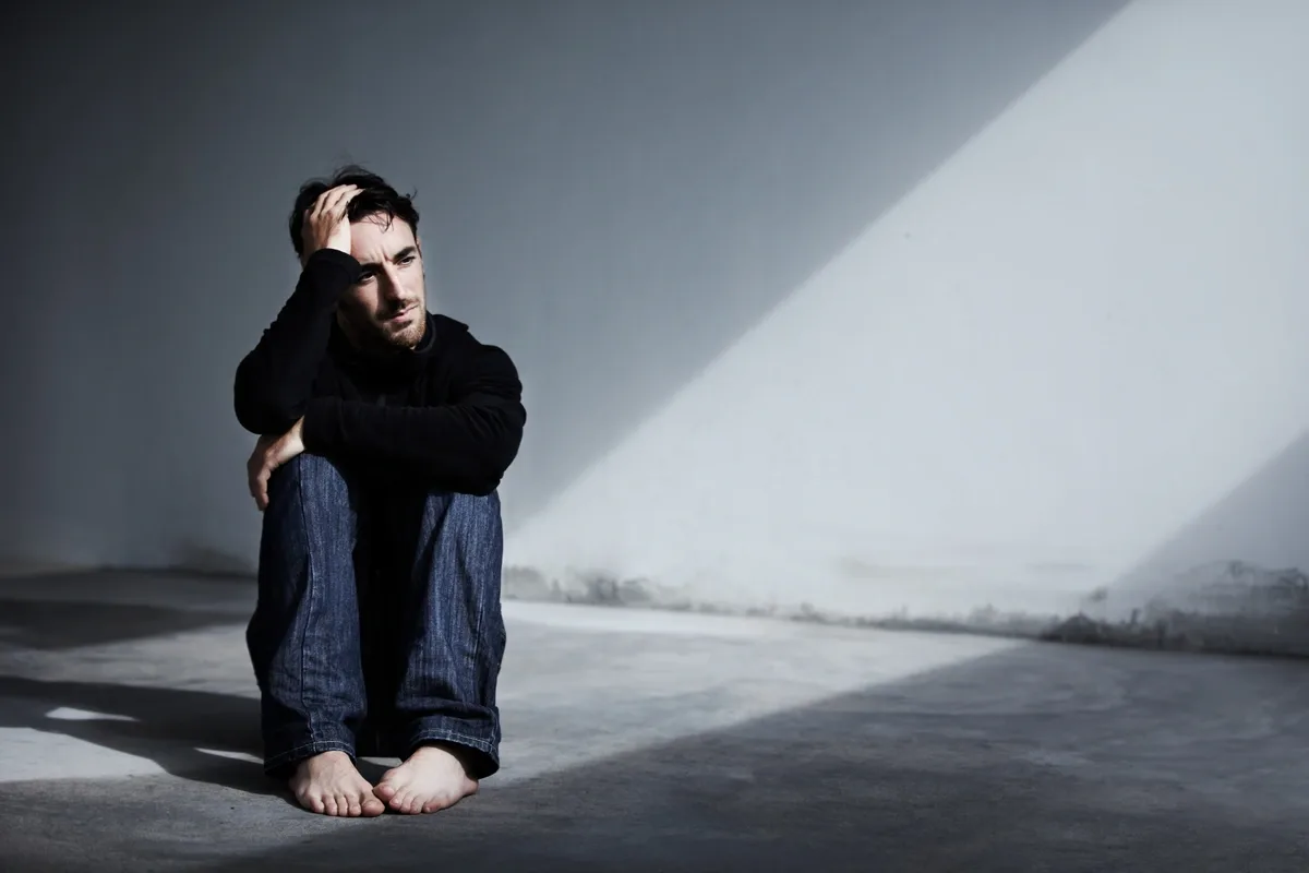 Depressed man sitting barefoot on the floor