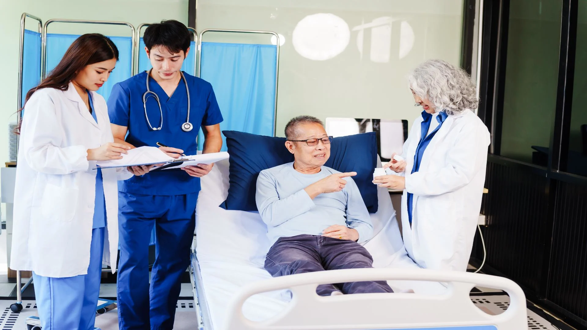 a female doctor examines an elderly asian man lying in hospital bed while nurses and doctors compare notes.