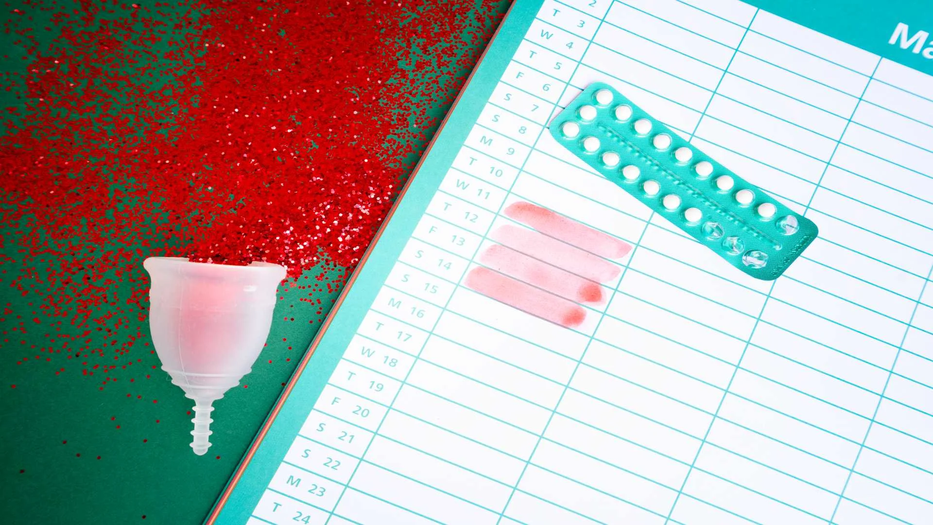 Menstrual cup, red glitter resembling blood, calendar marked for menstrual cycle, and birth control pills — representing PMDD tracking and hormonal self-care.