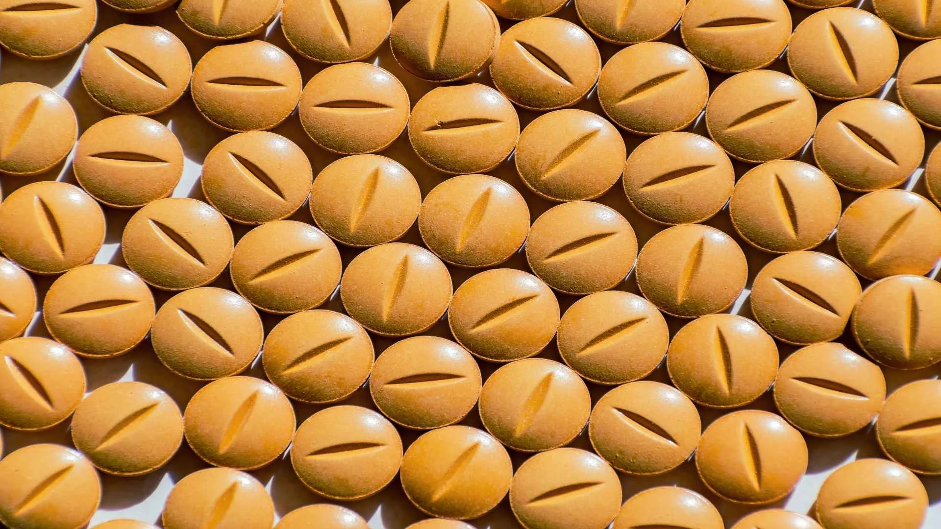 Macro shot of numerous yellow prescription Adderall pills with scored lines, arranged closely together.