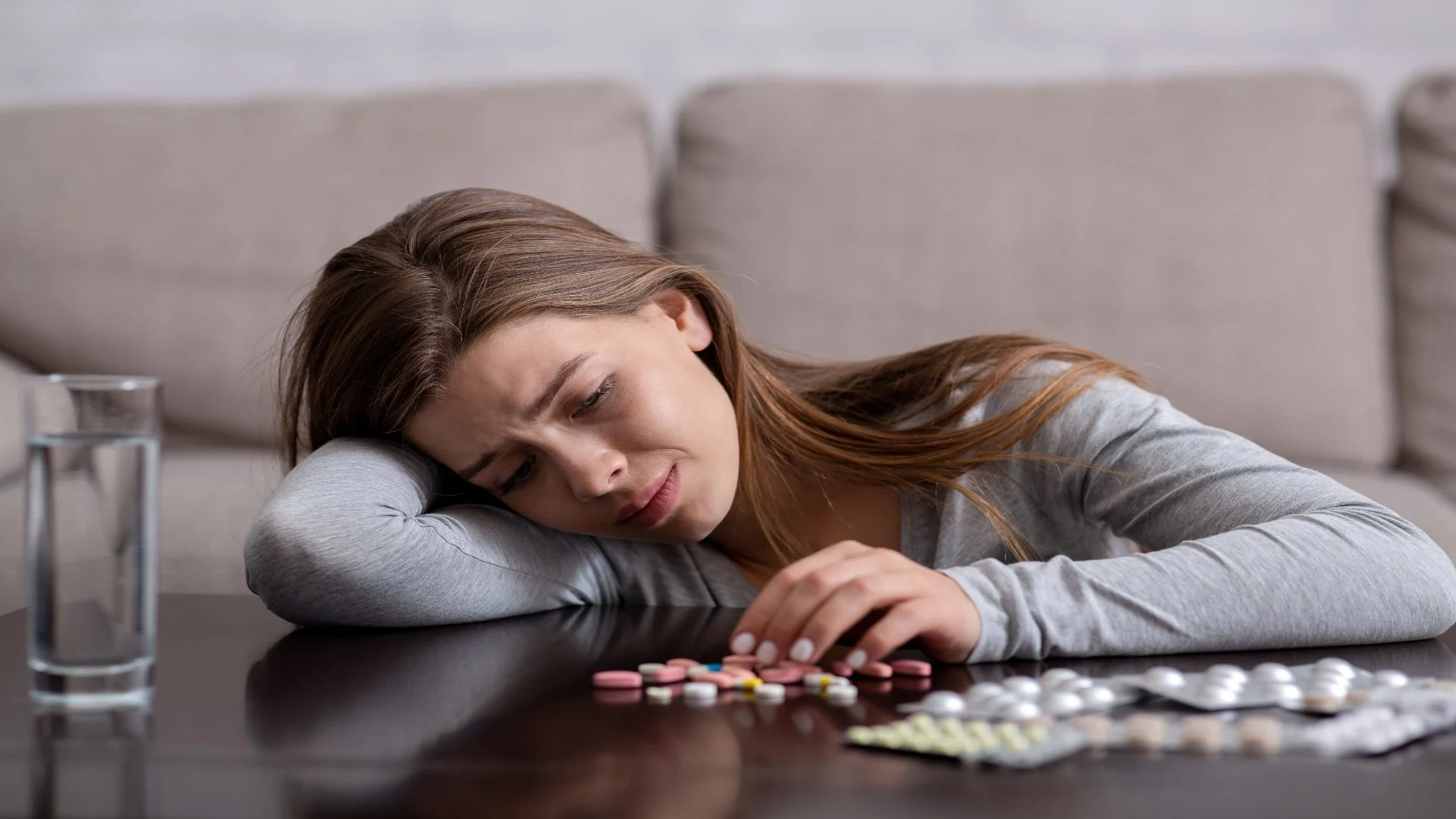 Synthetic opioids spread on a table with a sad young woman looking at them, symbolizing struggle with dependence.
