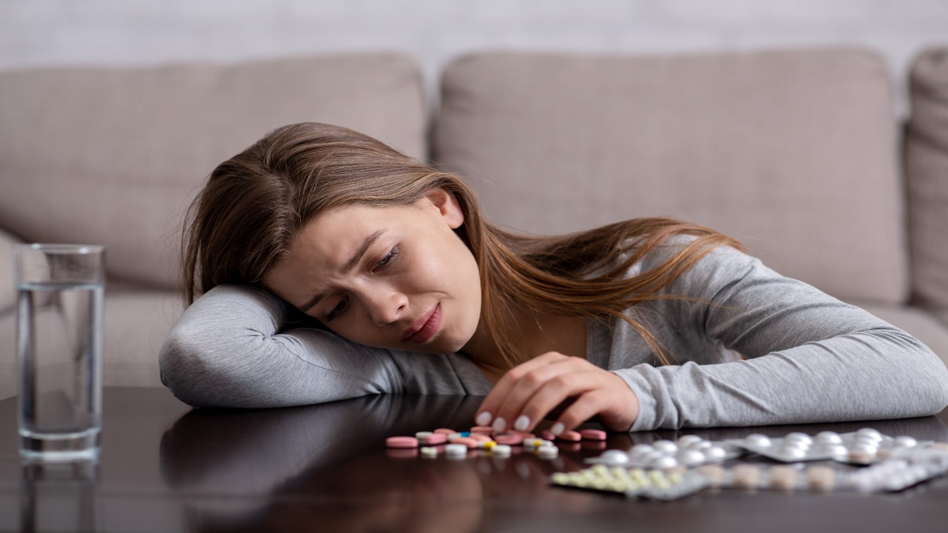 Synthetic opioids spread on a table with a sad young woman looking at them, symbolizing struggle with dependence. Synthetic opioids spread on a table with a sad young woman looking at them, symbolizing struggle with dependence.