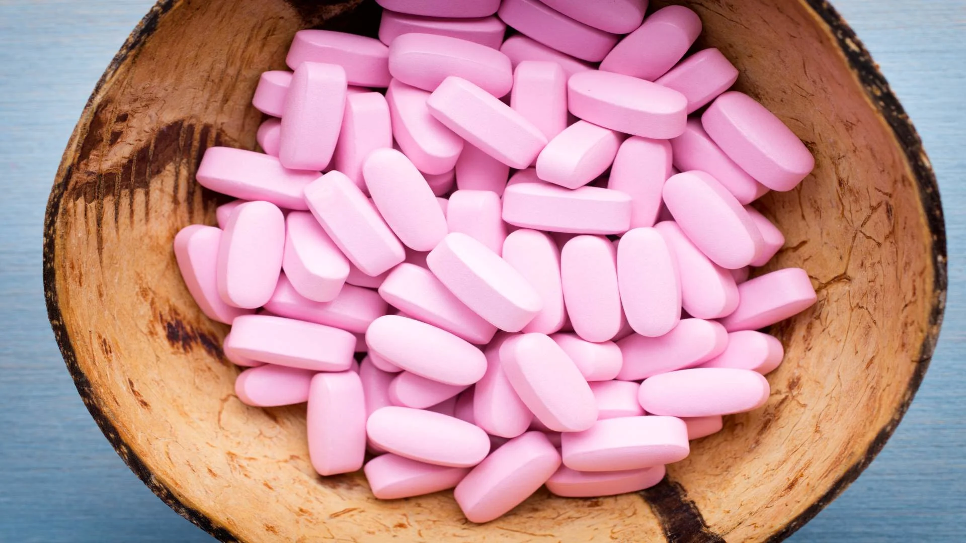 Pink pill supplements grouped in a rustic wooden bowl, suggesting over-the-counter usage appeal.