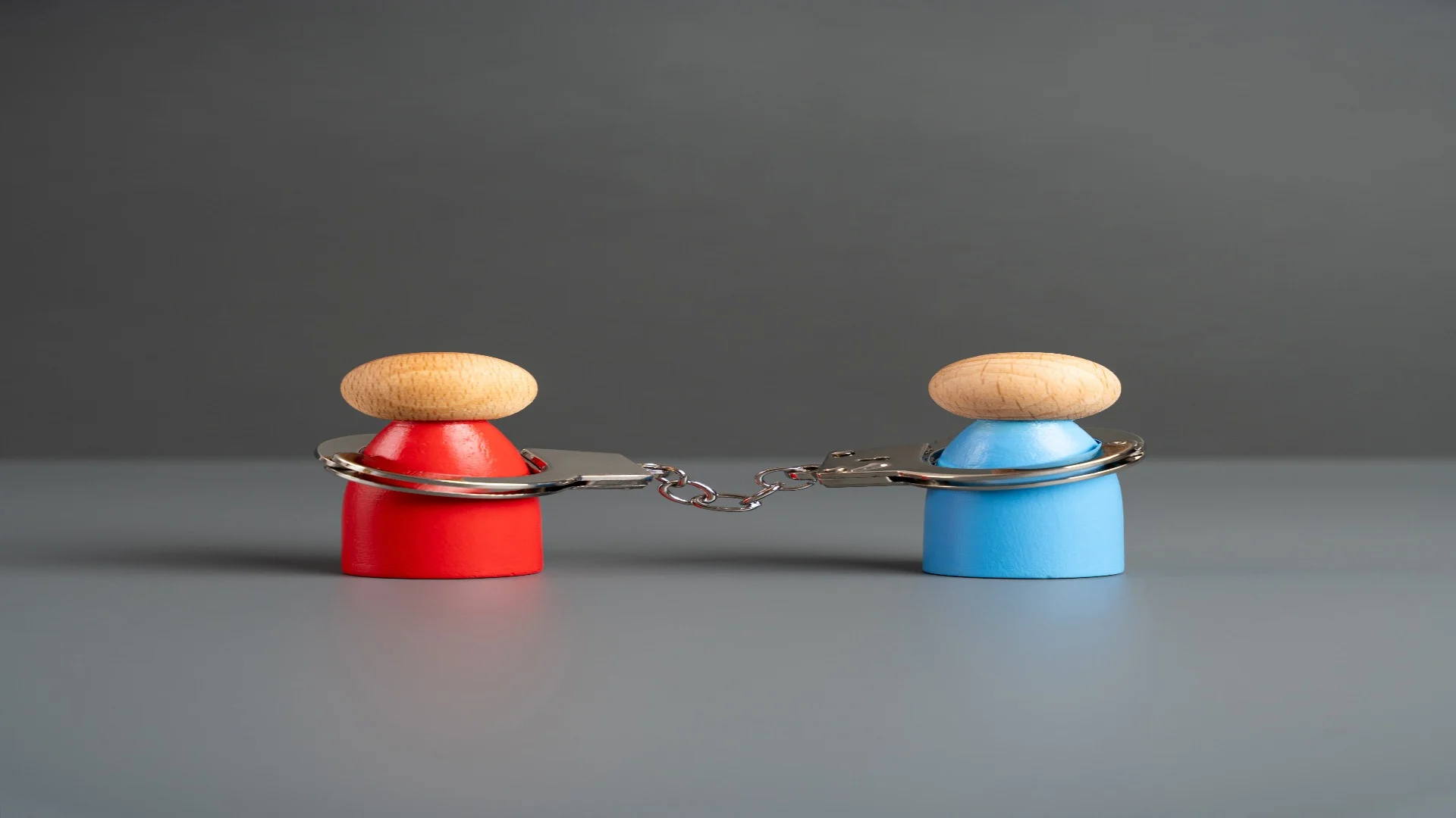 Wooden figures in red and blue connected by handcuffs symbolizing attachment issues and emotional dependency.