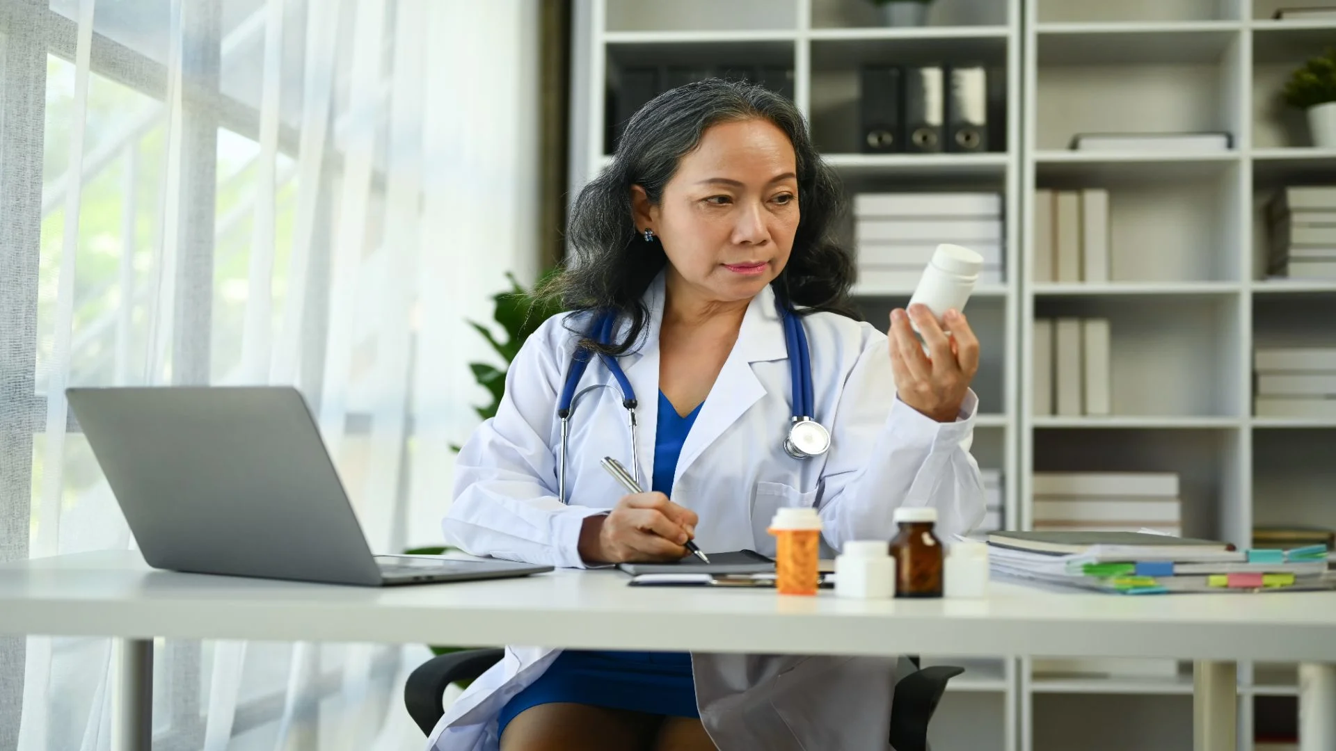 mature female doctor in white uniform holding a bottle of pregabalin comparing it to gabapentin