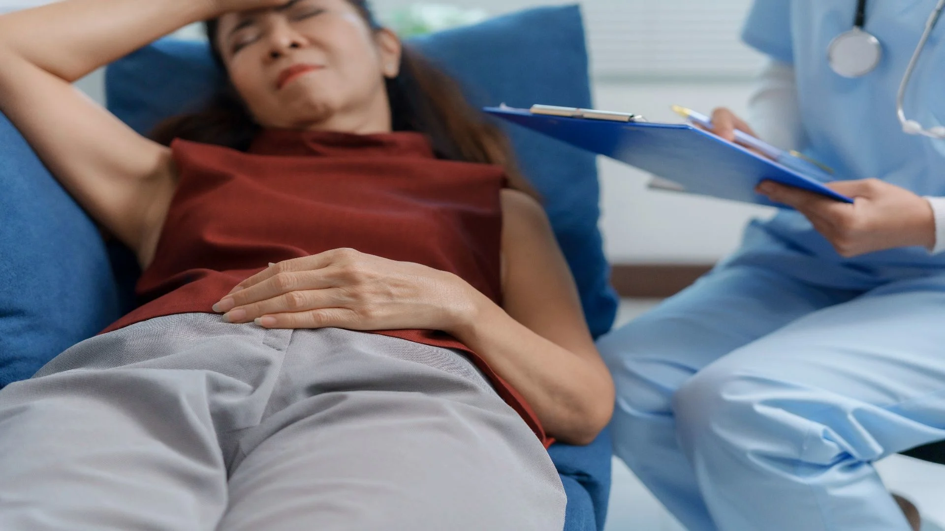 Woman experiencing abdominal pain while consulting a healthcare provider — a common symptom of premenstrual dysphoric disorder requiring medical support.
