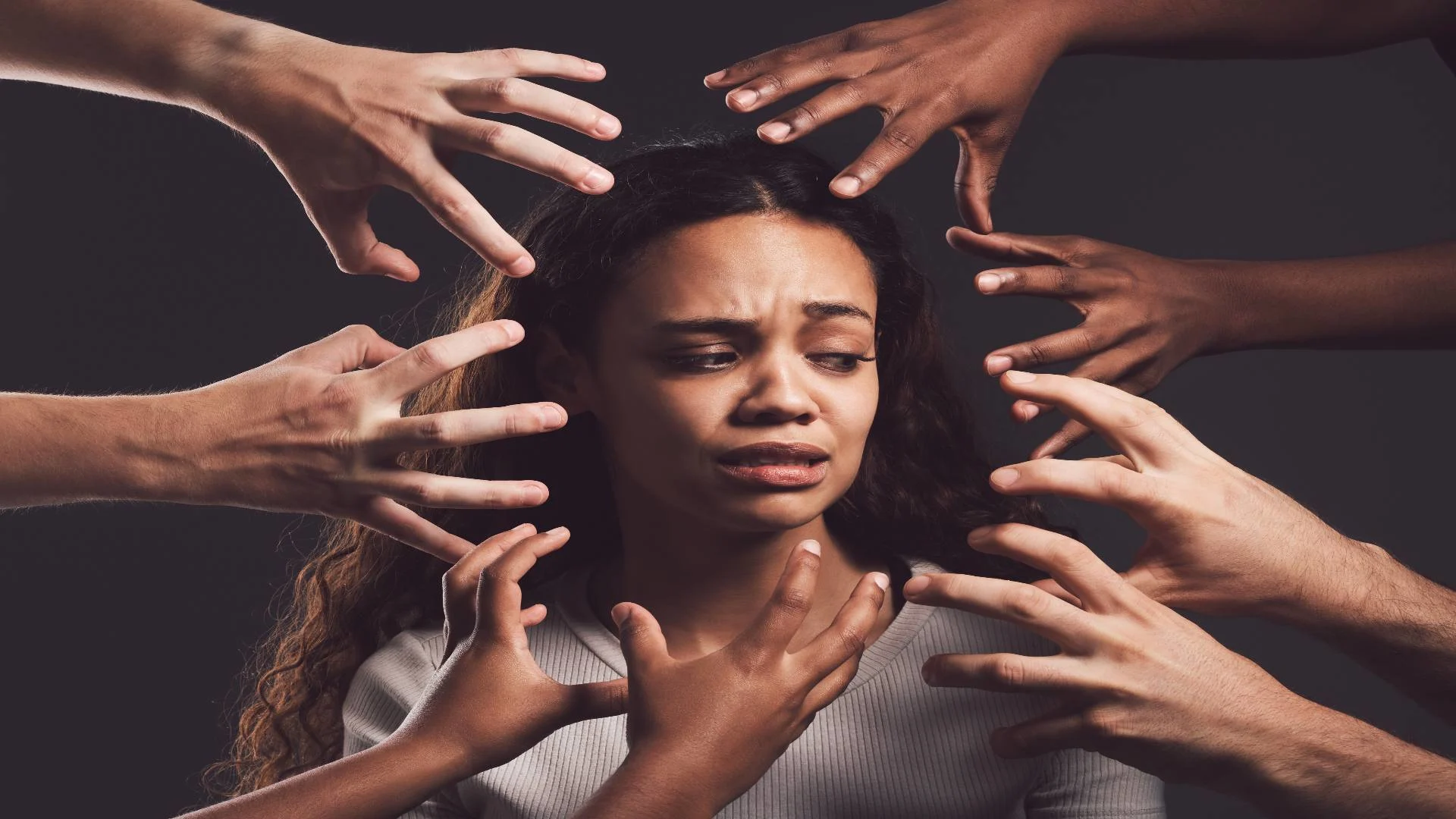 Distressed woman surrounded by grasping hands, symbolizing the overwhelming fear and pressure experienced during a panic or anxiety attack.
