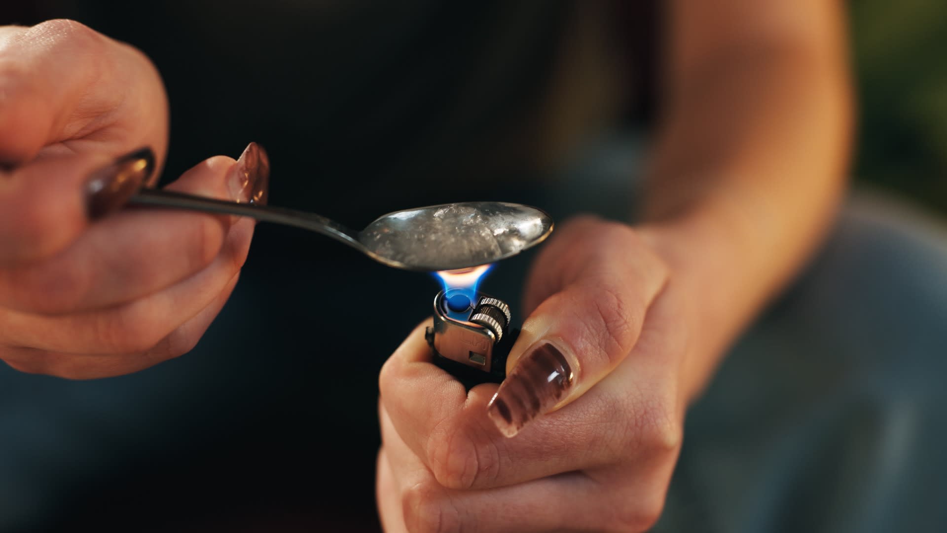 A close-up of a person holding a spoon over a lighter to prepare drugs, illustrating dangerous drug use behaviors. This image is relevant when exploring drug classifications and answering questions like "is meth an opioid."