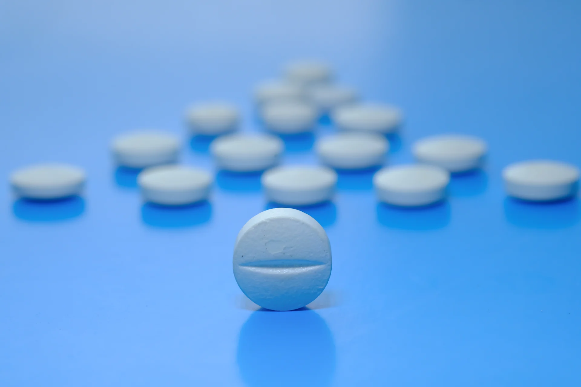 White round pills on a blue background with one in focus, symbolizing the question 'Is Valium a Narcotic'.
