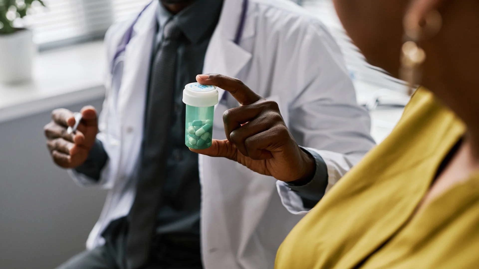 close up of doctors hand holding a bottle of pills discussing the effects with a patient