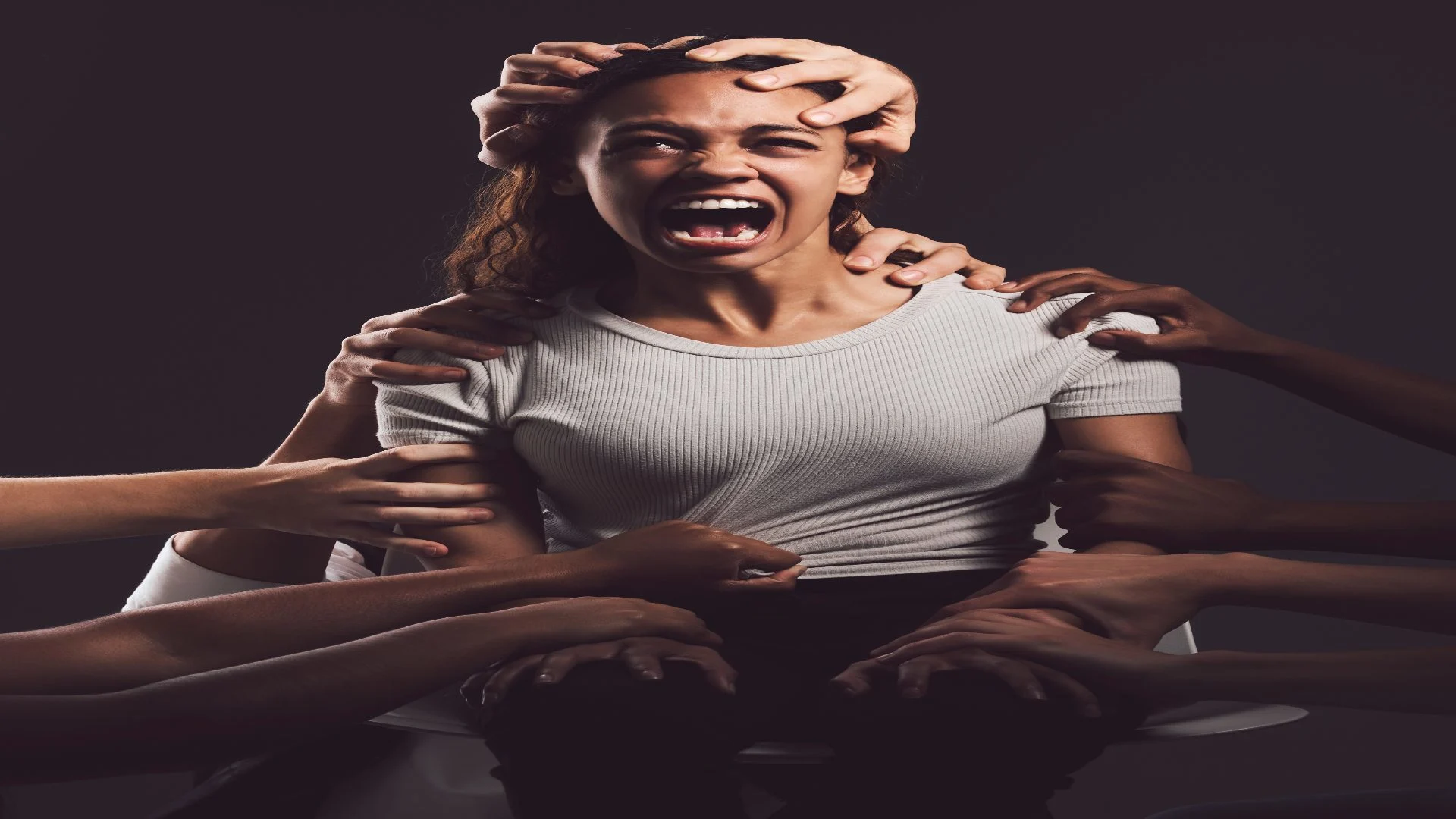 Young woman screaming as multiple hands reach for her, visually expressing the inner turmoil and hallucinations that can define what schizophrenia is.
