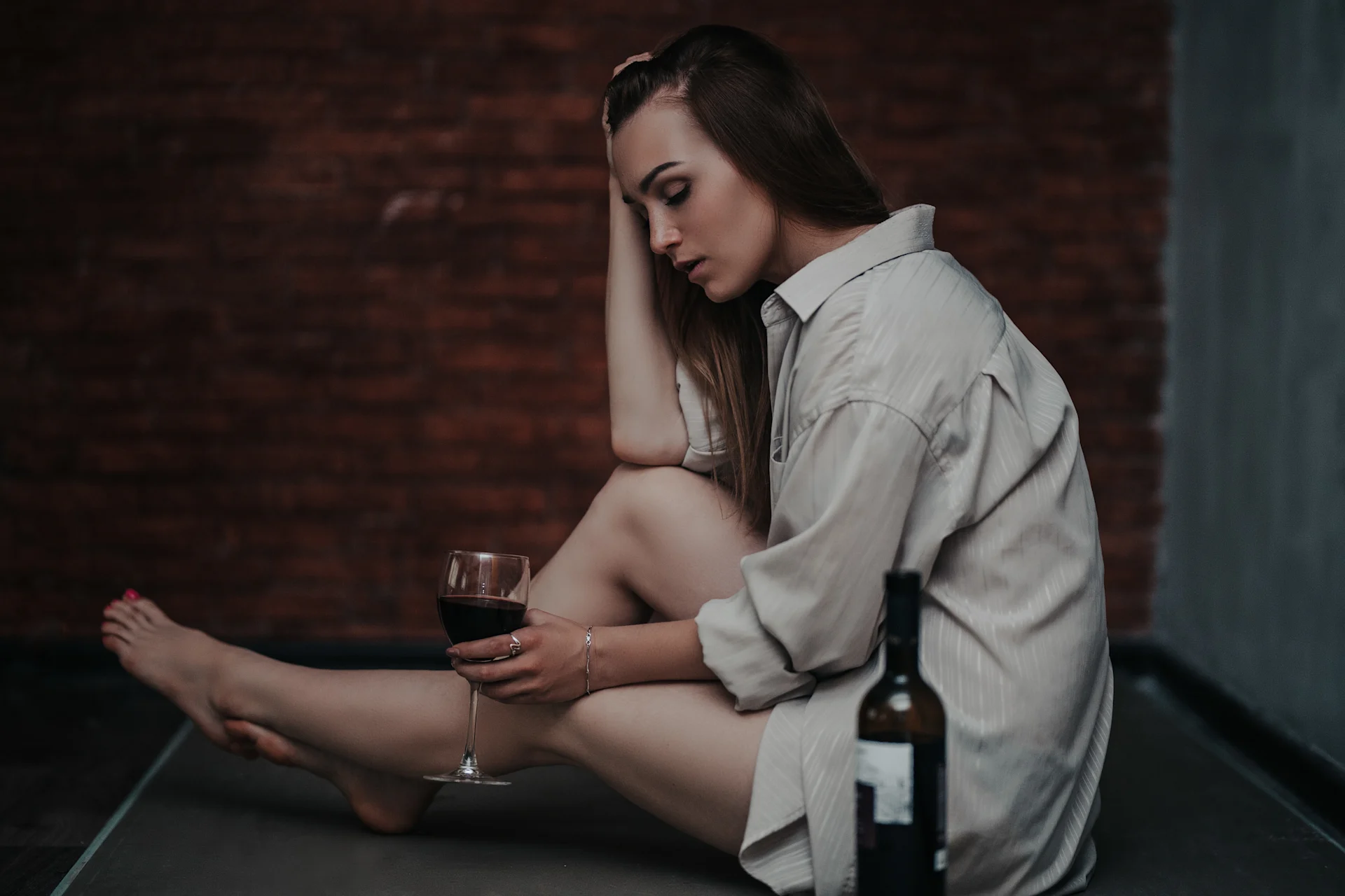 Sad woman sitting on the floor with a glass of wine, symbolizing the struggle between addiction as a disease or choice.