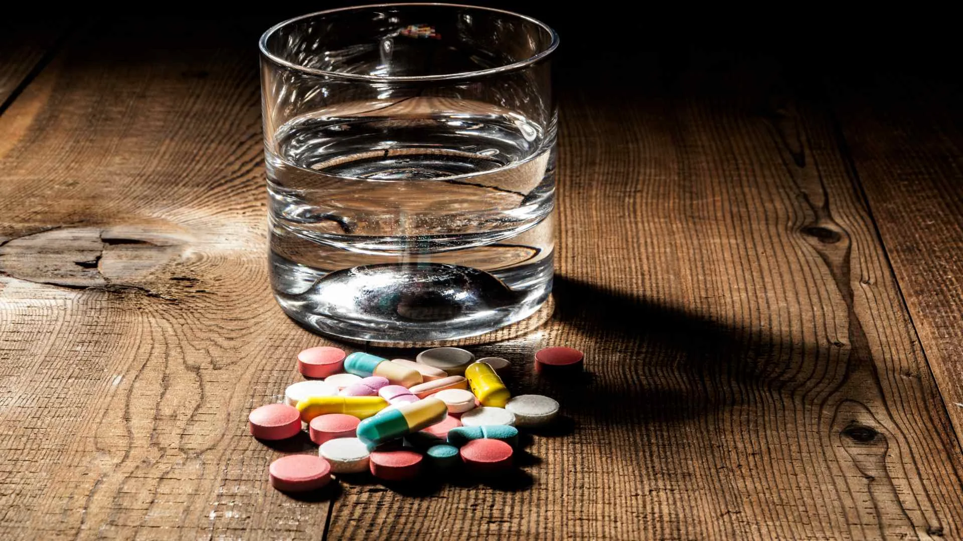 Assorted colorful pills beside a glass of water on a wooden surface, representing medication such as Valium and its use in treatment.