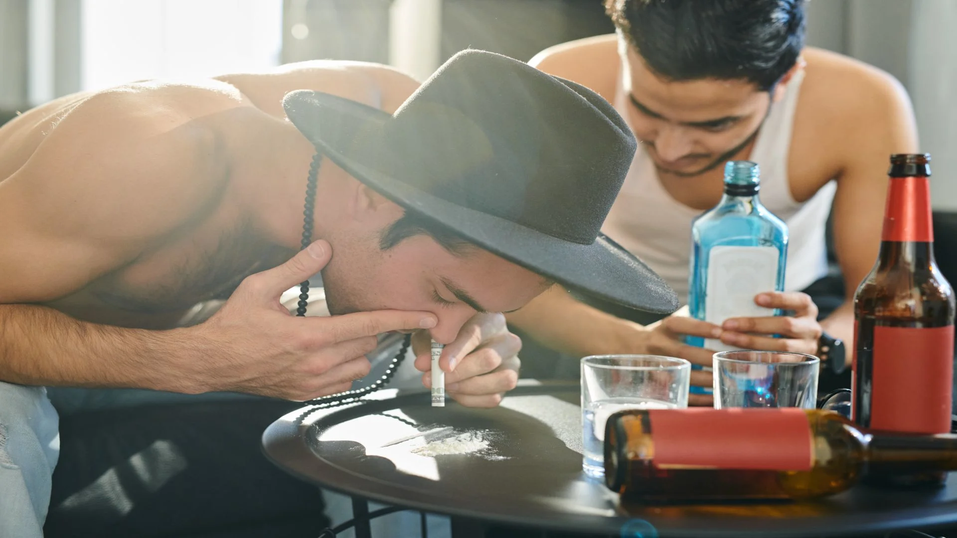 Man snorting a white powder next to bottles of alcohol, illustrating substance misuse in the context of ‘what is meth?’ and its dangers.