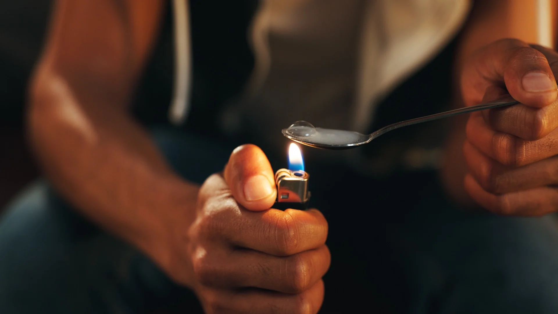 Close-up of hands heating a substance in a spoon over a lighter, visually depicting intravenous drug use related to what is meth.