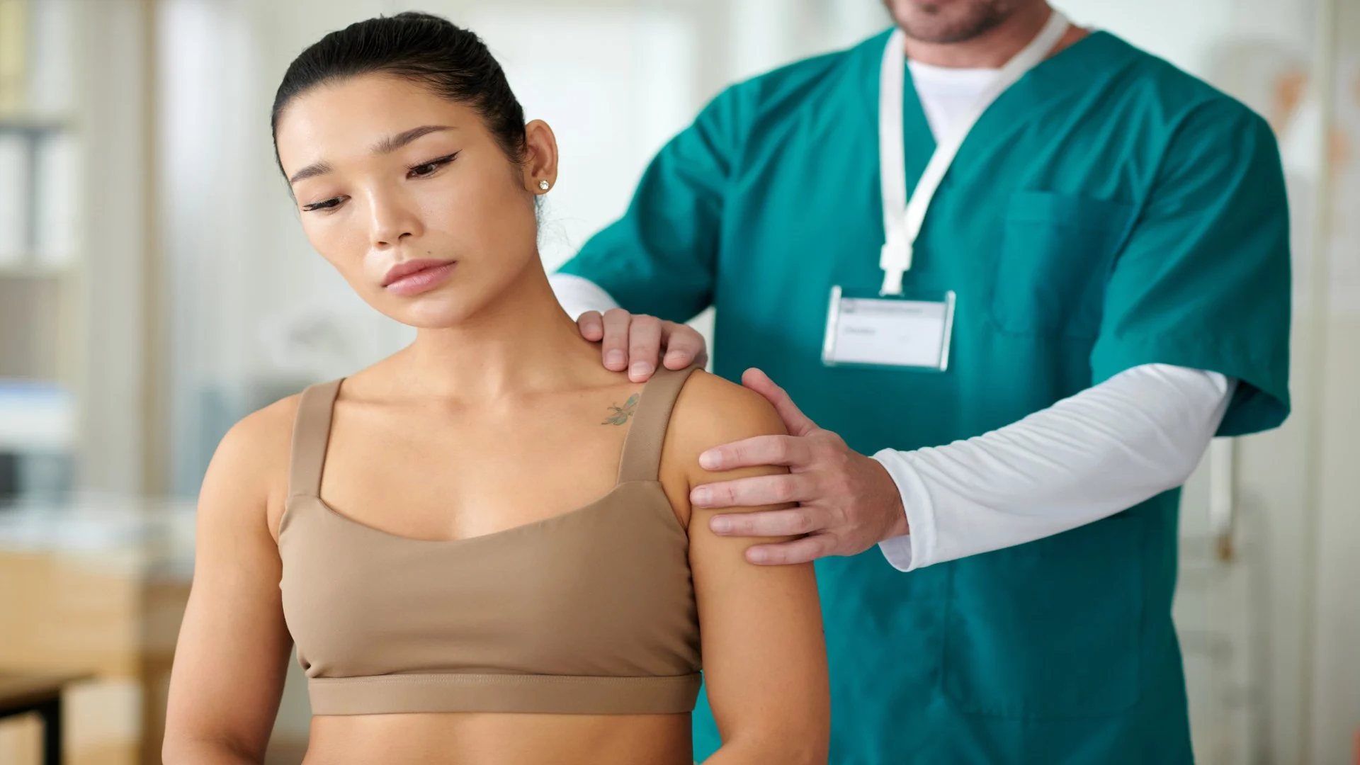 Asian woman in sports bra with shoulder pain getting a massage from a physical therapist