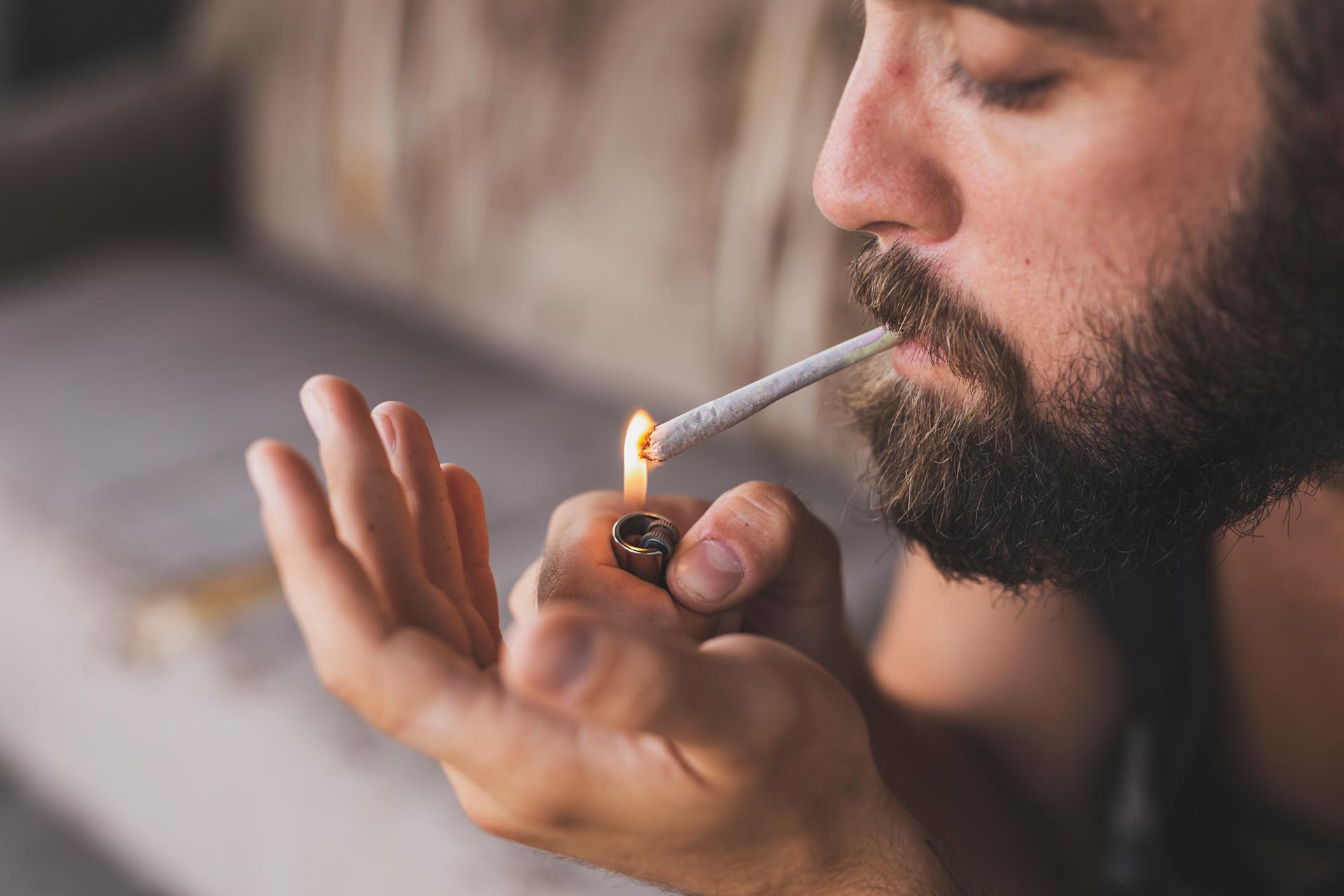 Bearded man lighting a joint with a lighter, highlighting the habitual use of marijuana and raising questions about whether marijuana is addictive.
